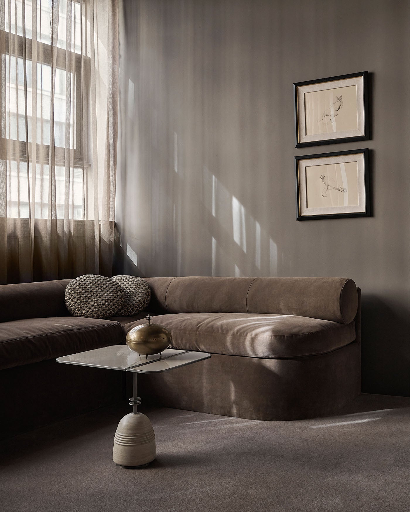 Minimalist living room corner with a curved brown sofa, textured round cushions, and a modern side table with brass decor piece