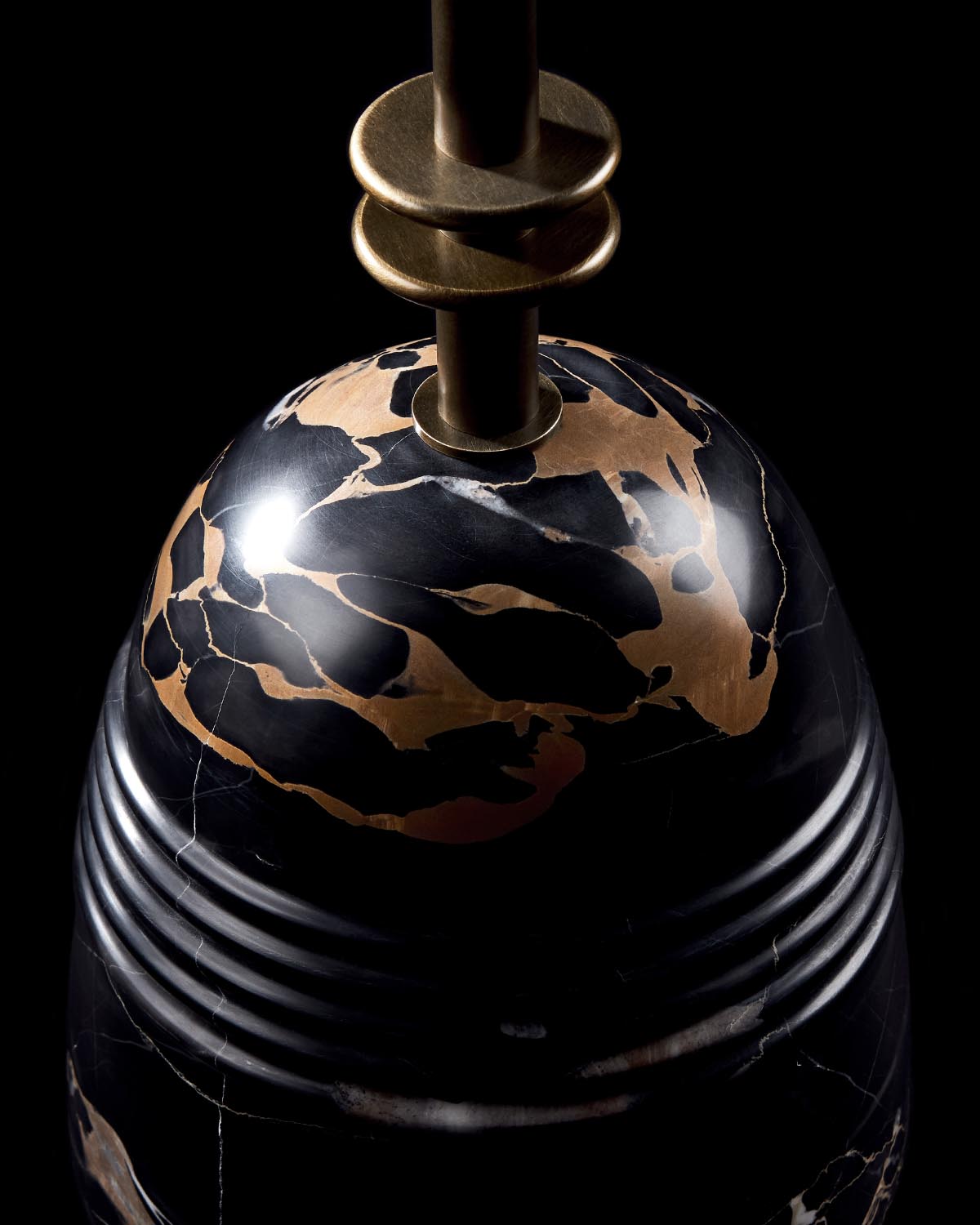 Close-up of a polished black and gold marble smoking table base with brass metal details on a black background