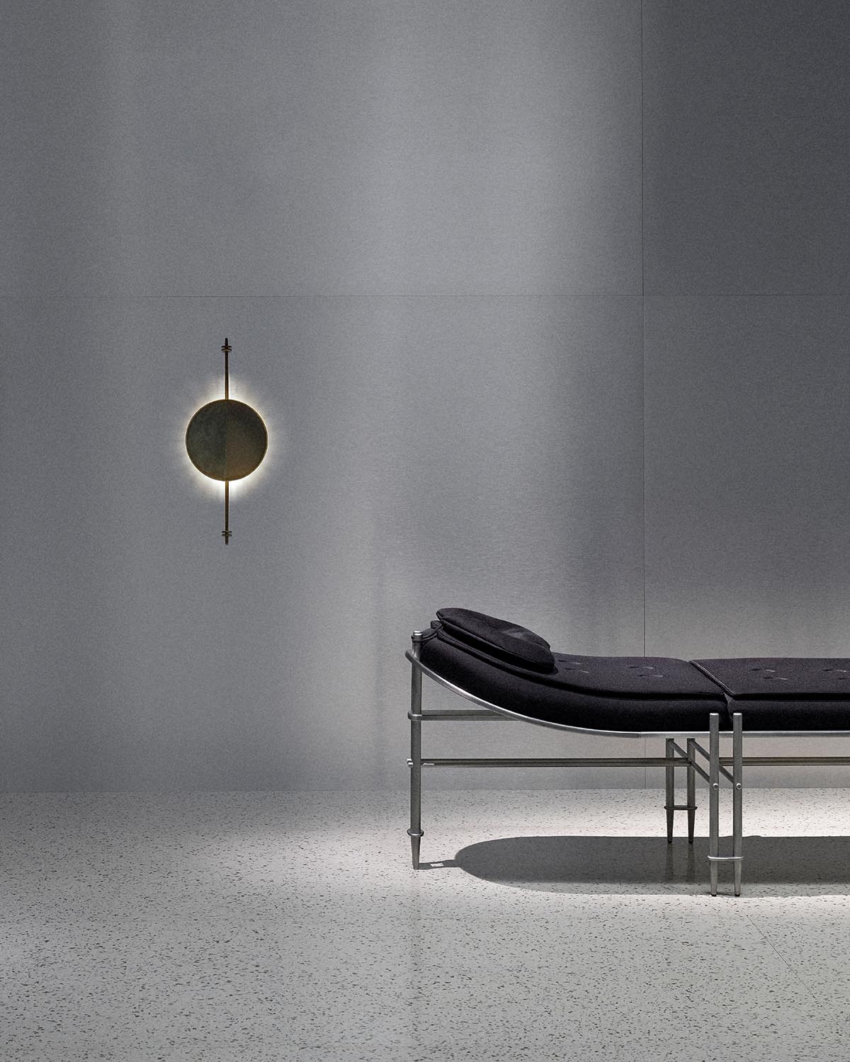 Minimalist wall sconce with circular light and vertical rod mounted on smooth gray wall above modern black lounge chair