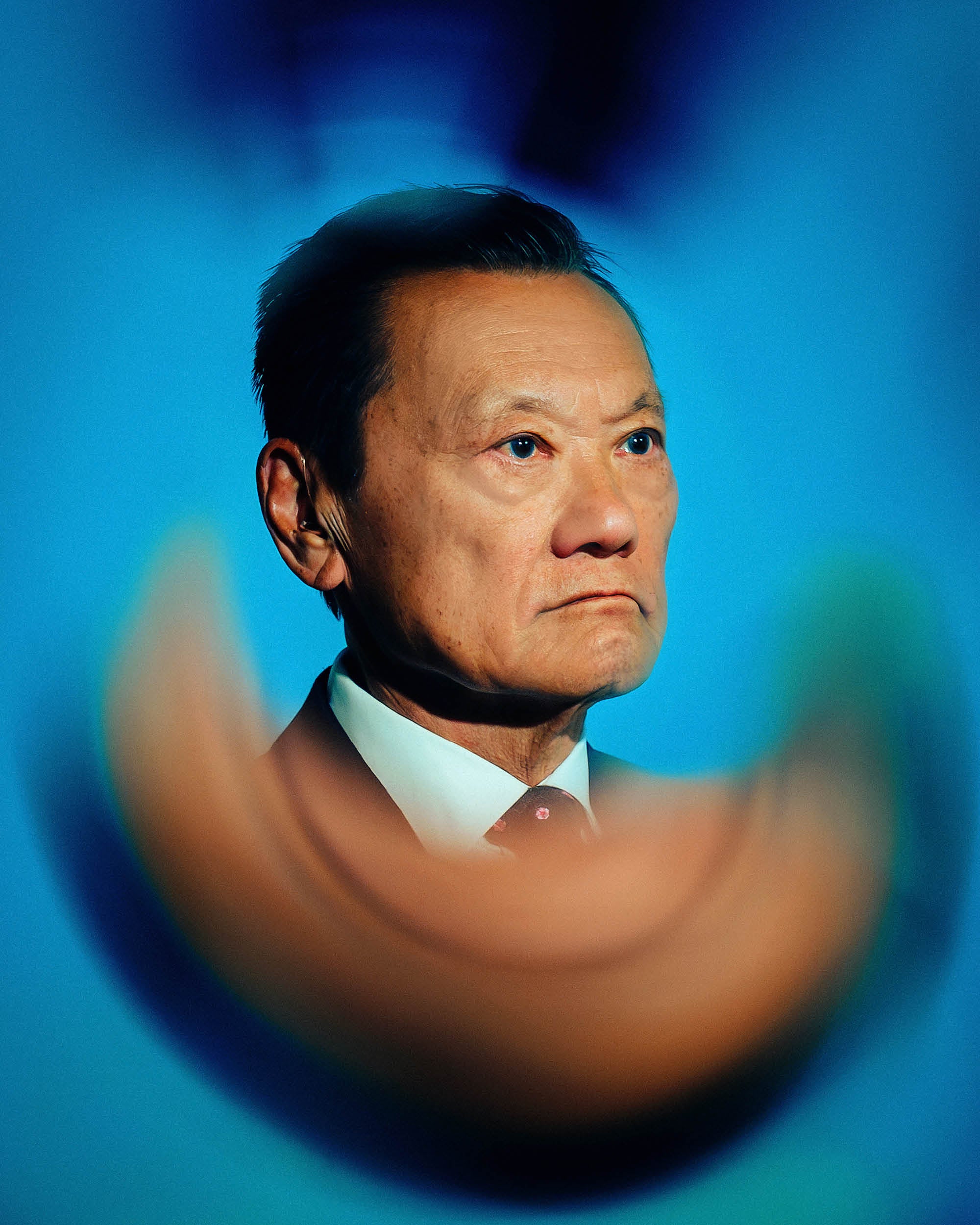 Portrait of a serious middle-aged man in a suit against a blurred blue background with abstract shapes.