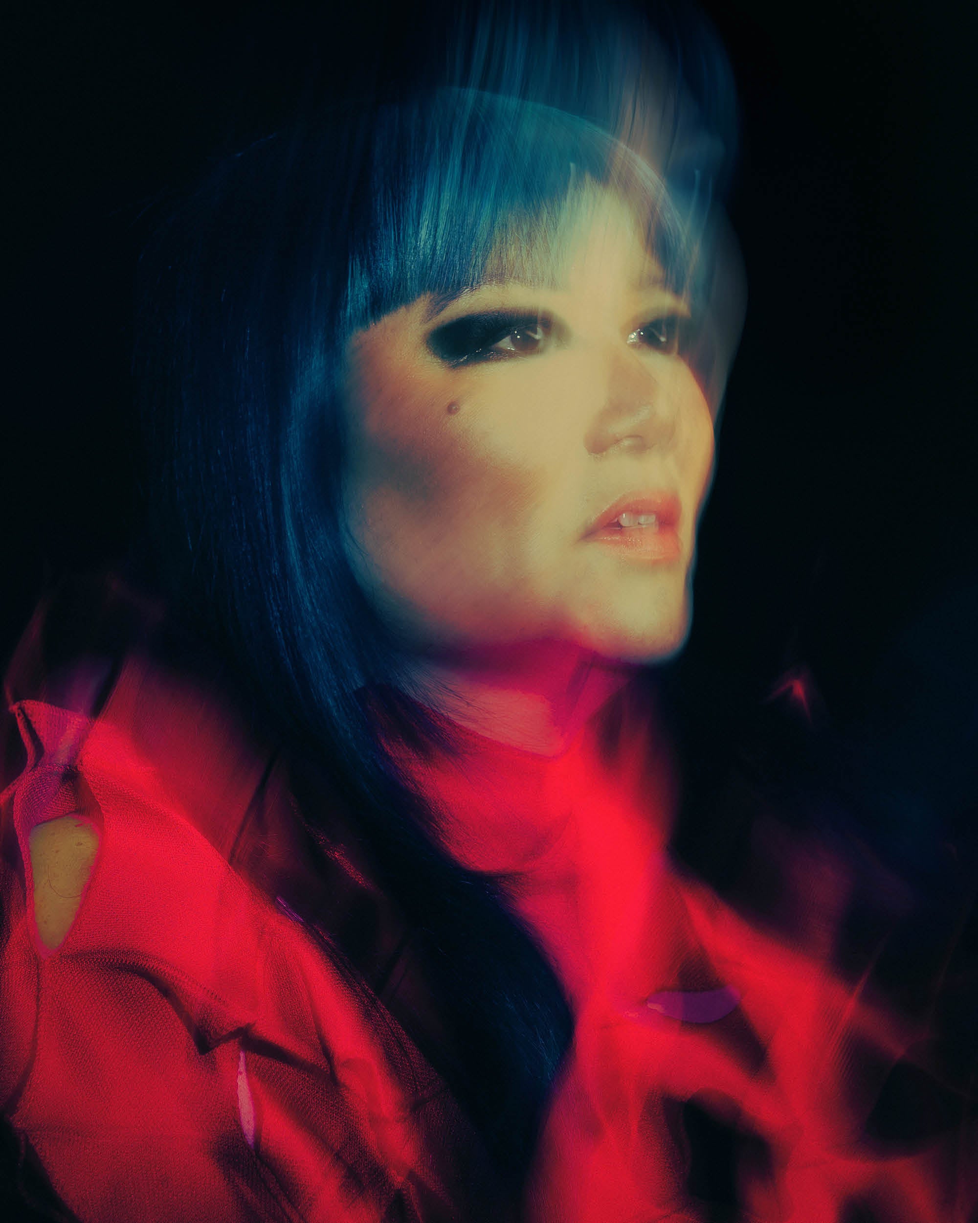 Blurred artistic portrait of a woman with dark hair and red clothing against a black background