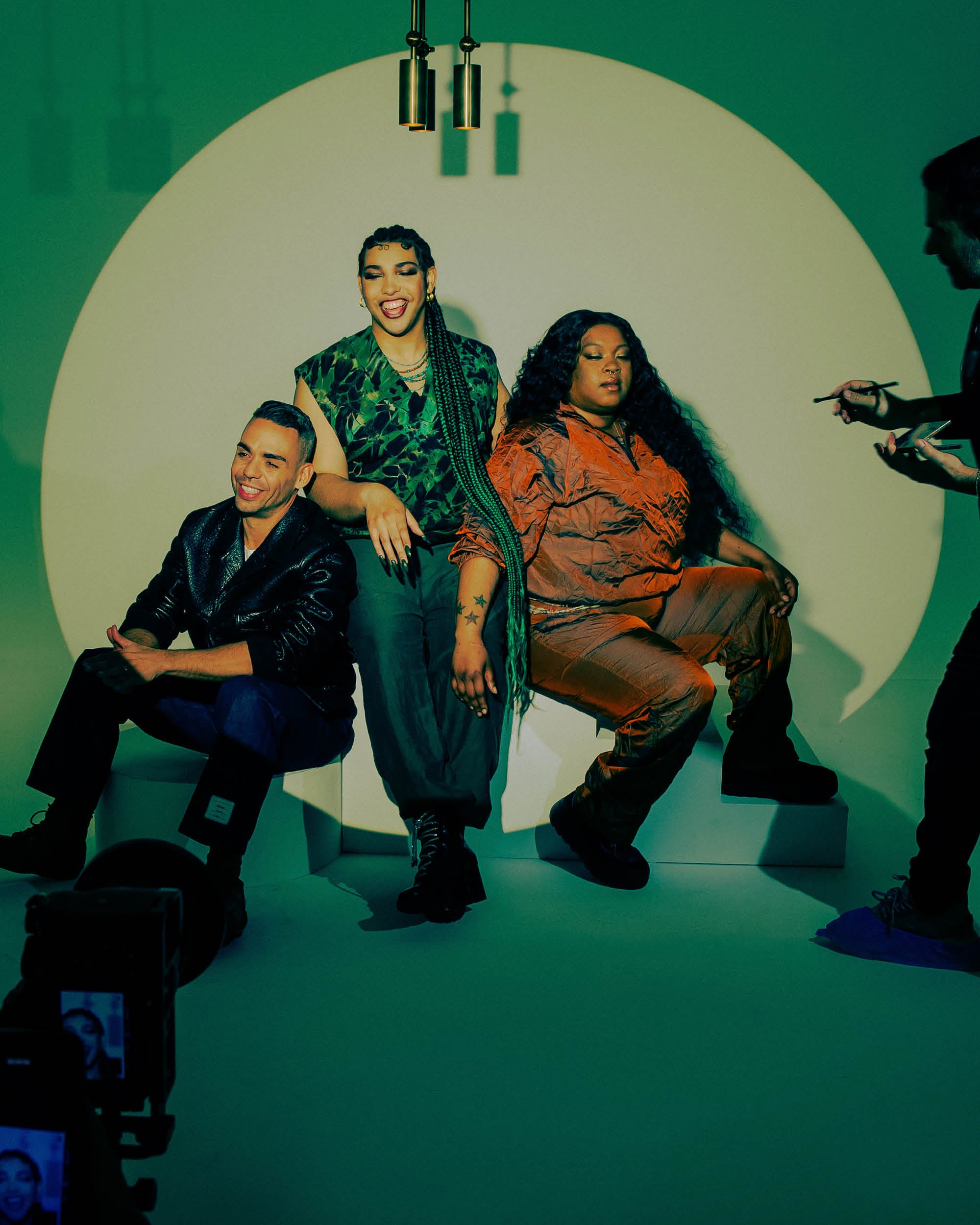 Three people posing against a large circular light backdrop with a photographer adjusting settings on the right side