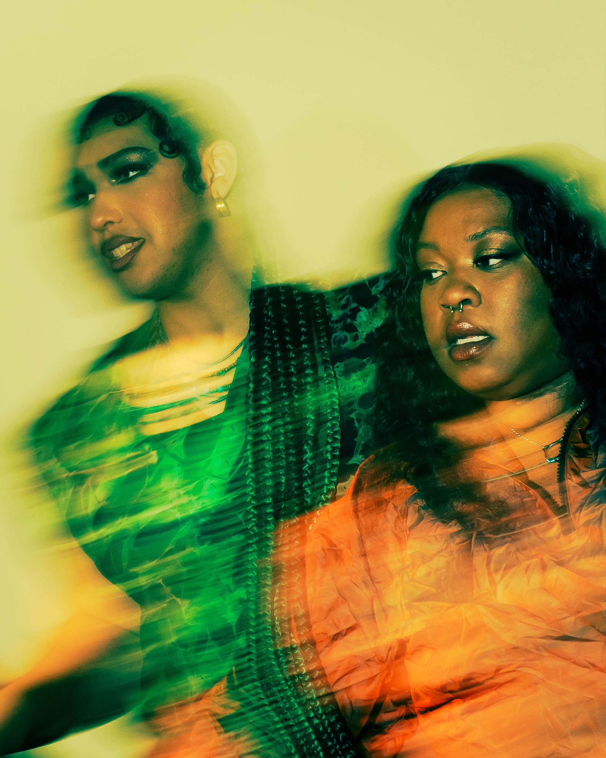 Portrait of two people with blurred motion effect, one wearing green and the other in orange, against a yellow background