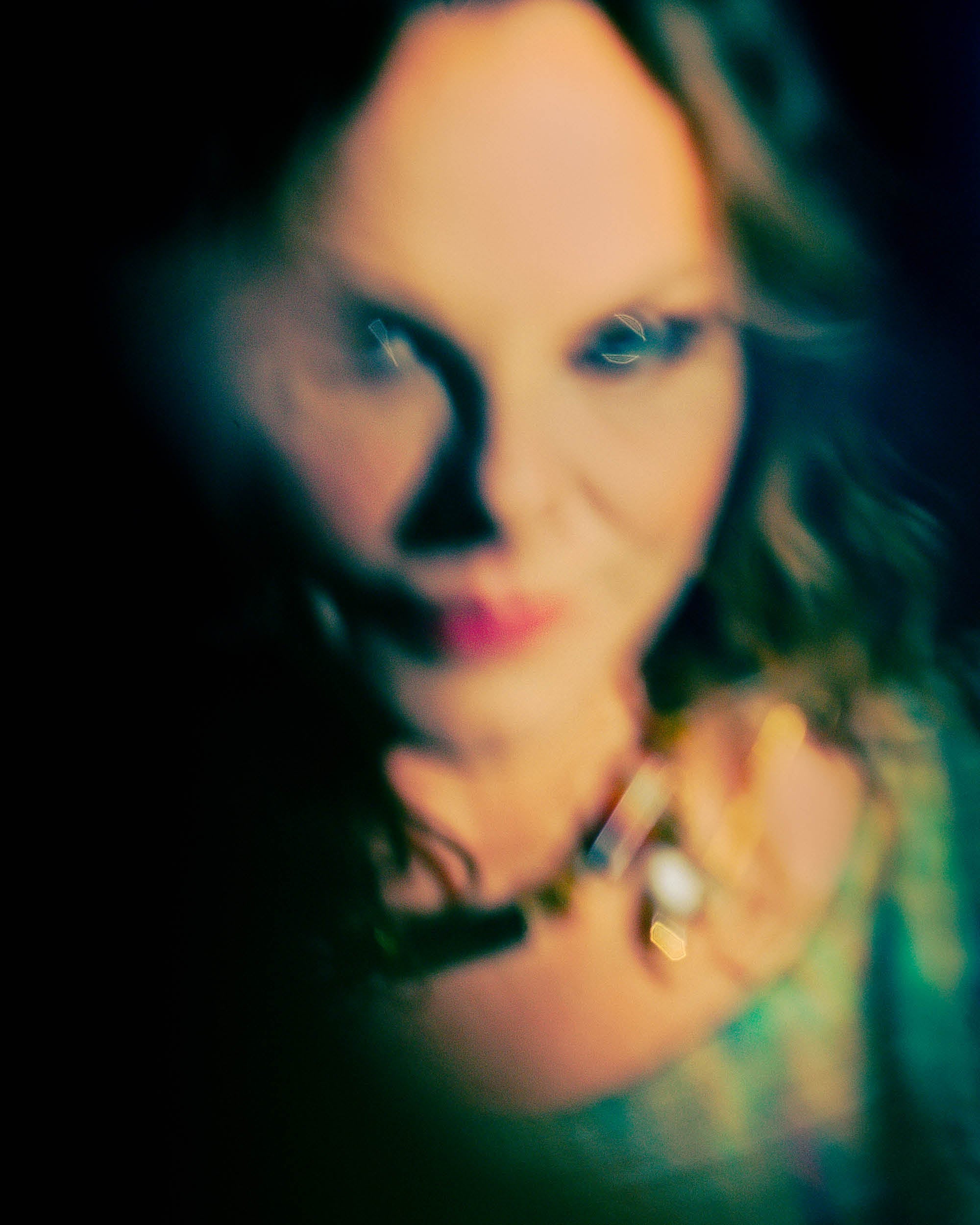 Blurred close-up of a woman with curly hair and a colorful top against a dark background