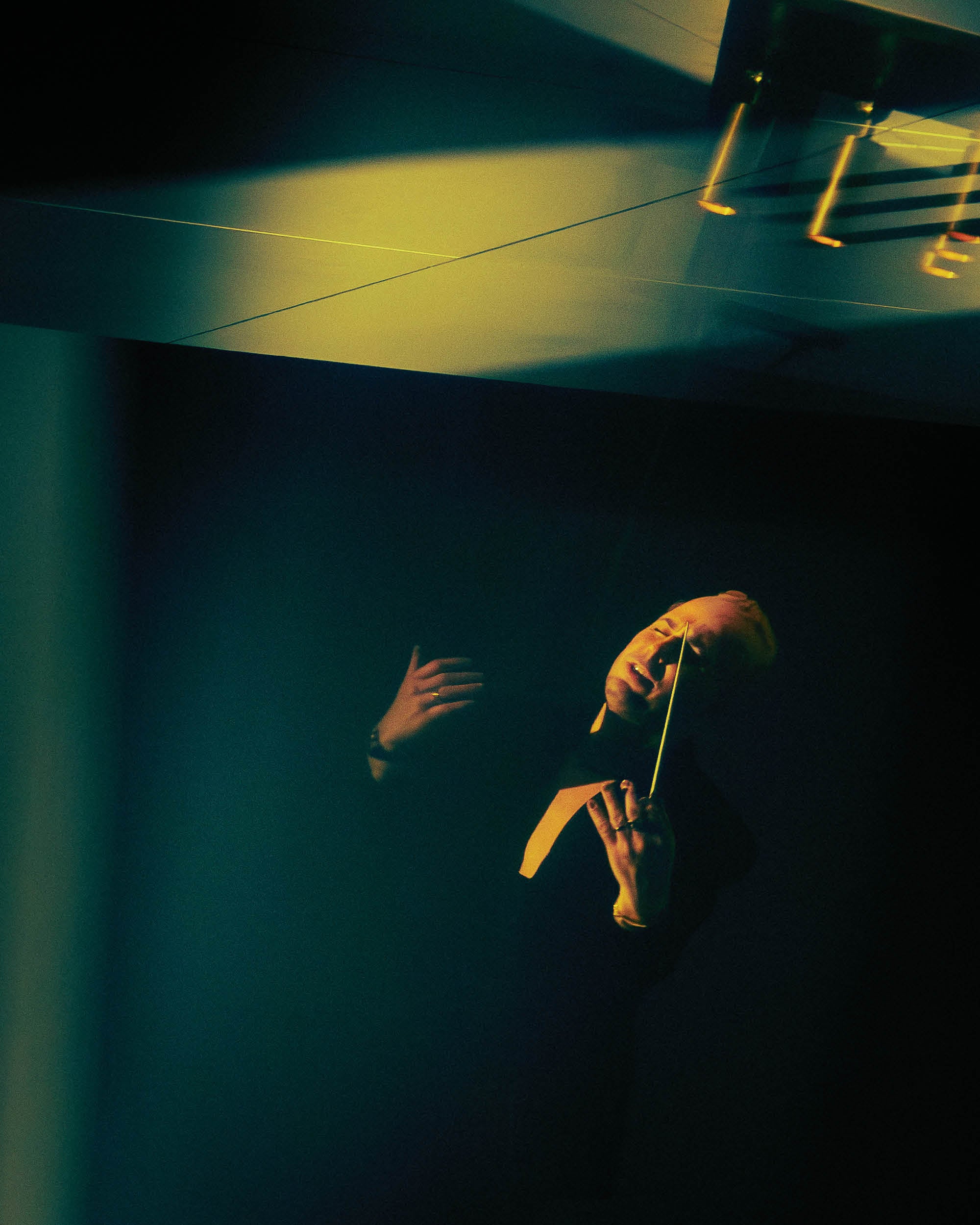 Dramatic low-light portrait of a conductor passionately leading with a baton against a dark background