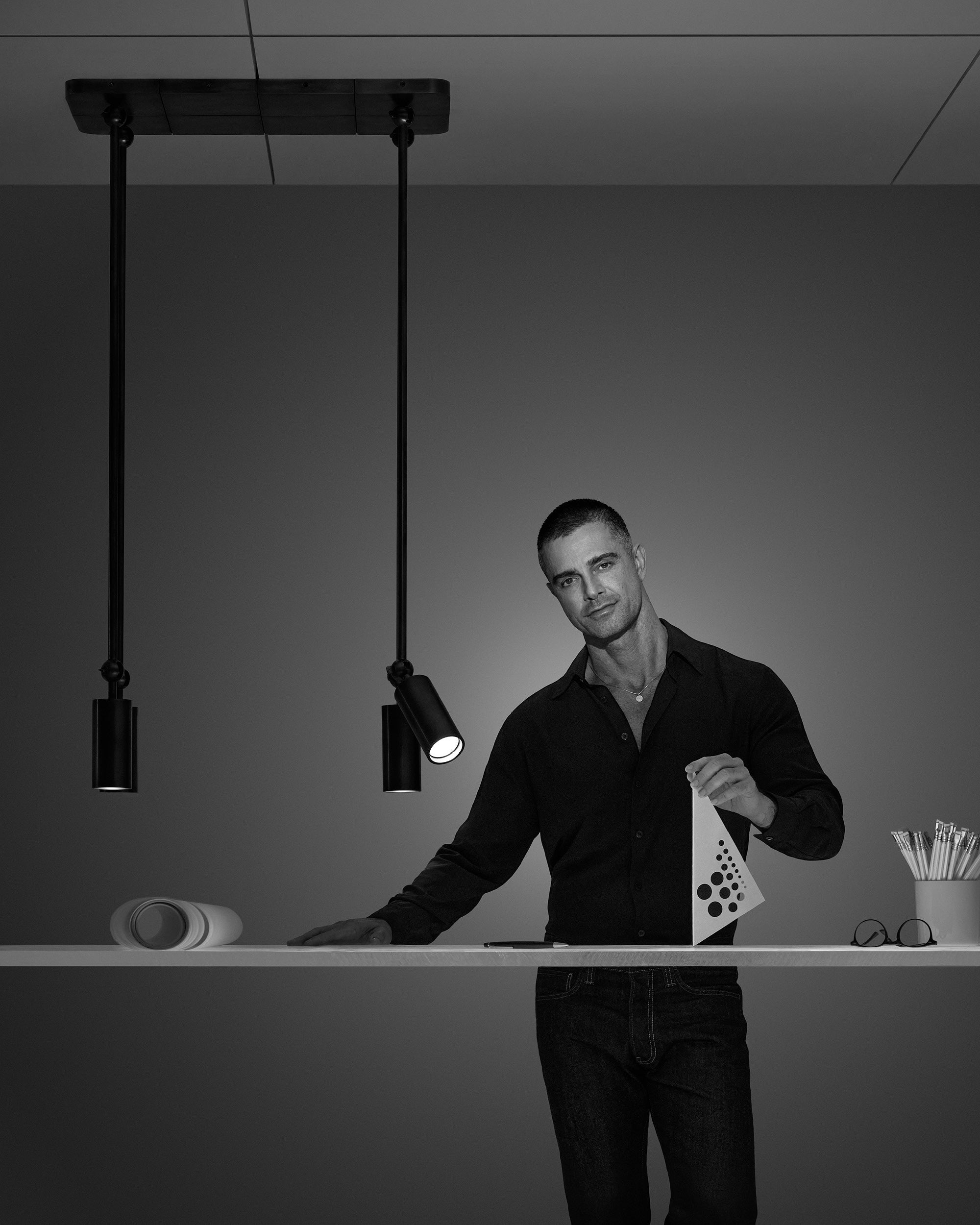Black and white image of a man standing behind a white counter under two modern pendant lights against a plain background
