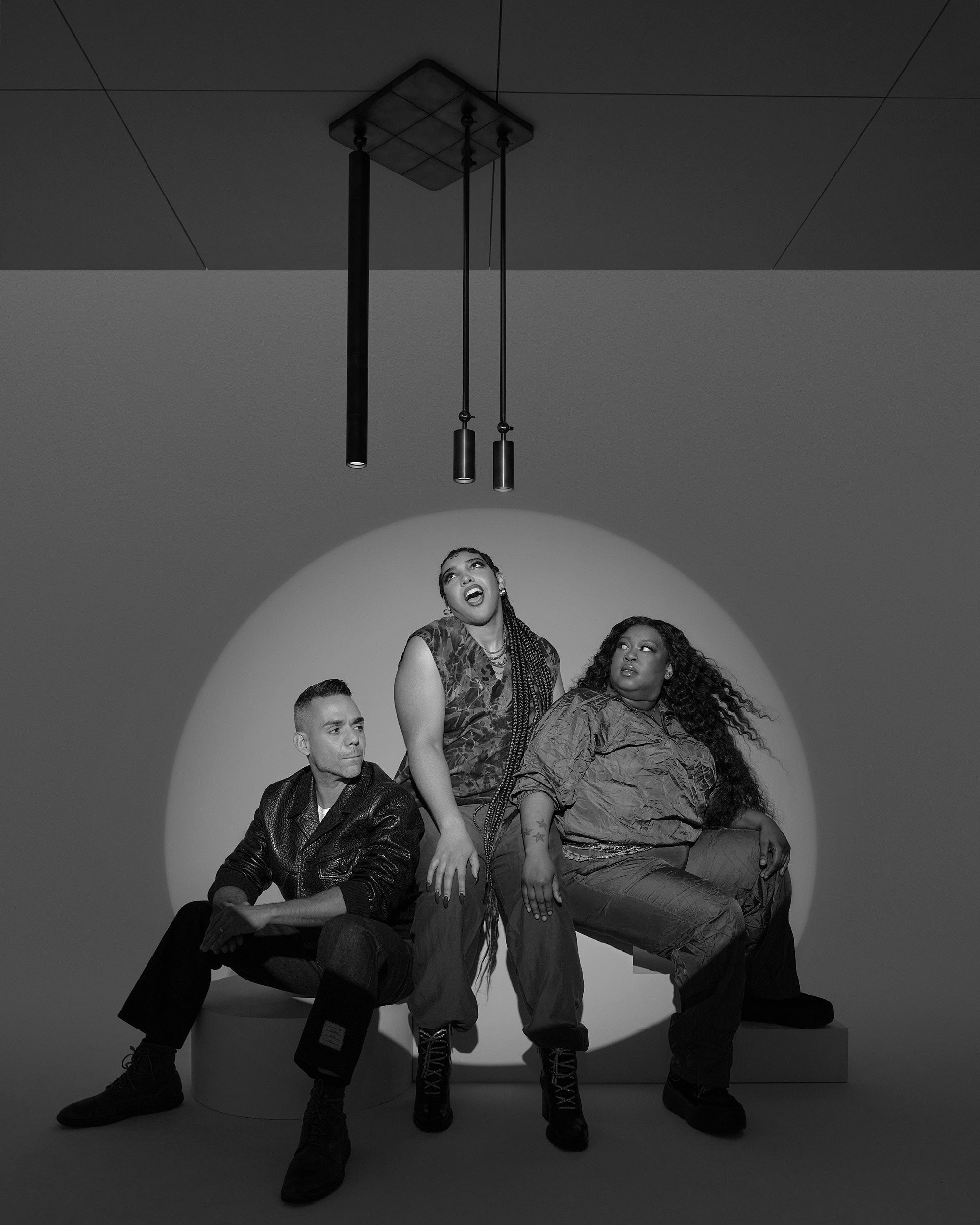 Black and white photo of three people posing with dramatic lighting and modern pendant lights overhead