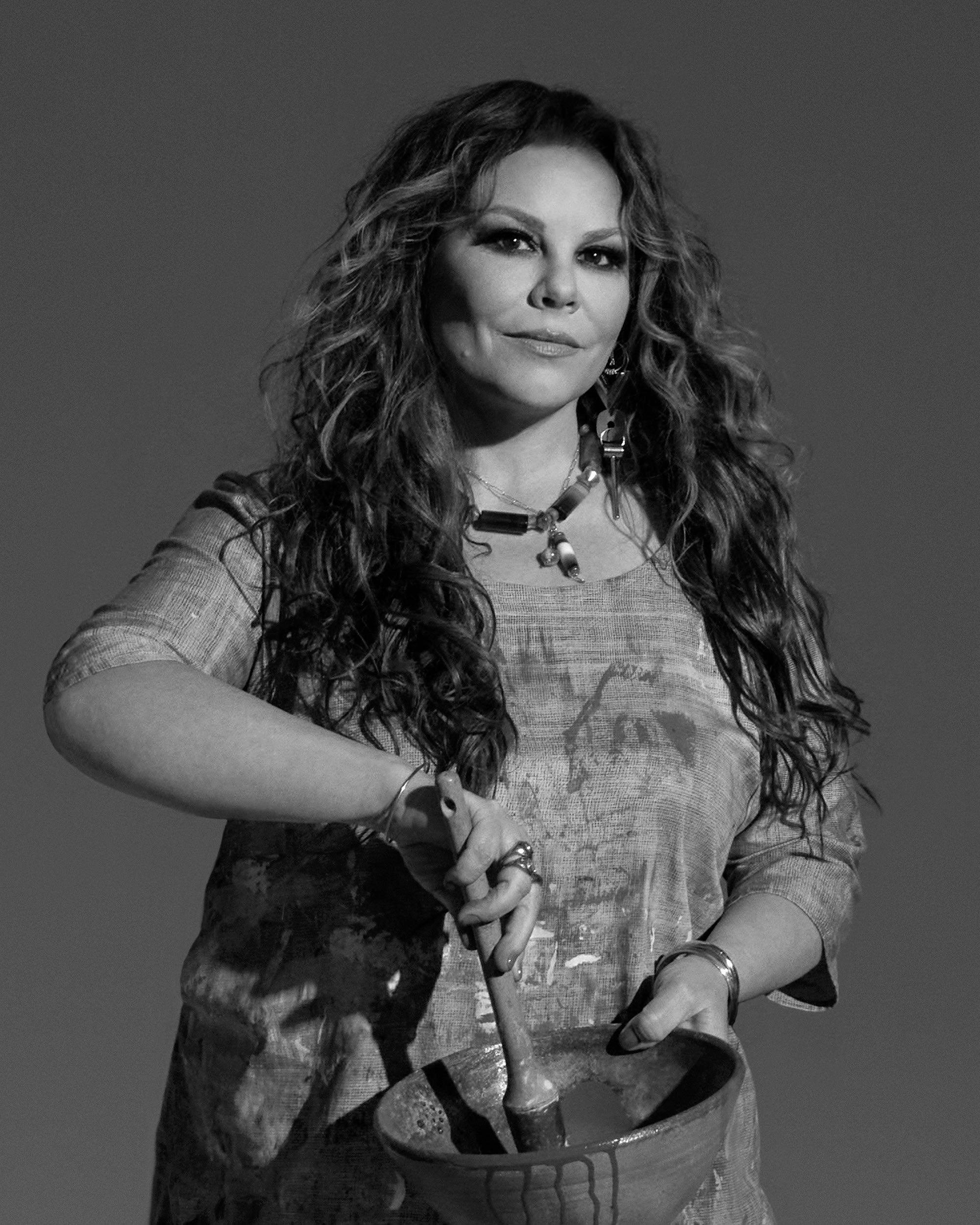 Black and white portrait of a woman with long wavy hair holding a wooden spoon in a ceramic bowl against a plain background