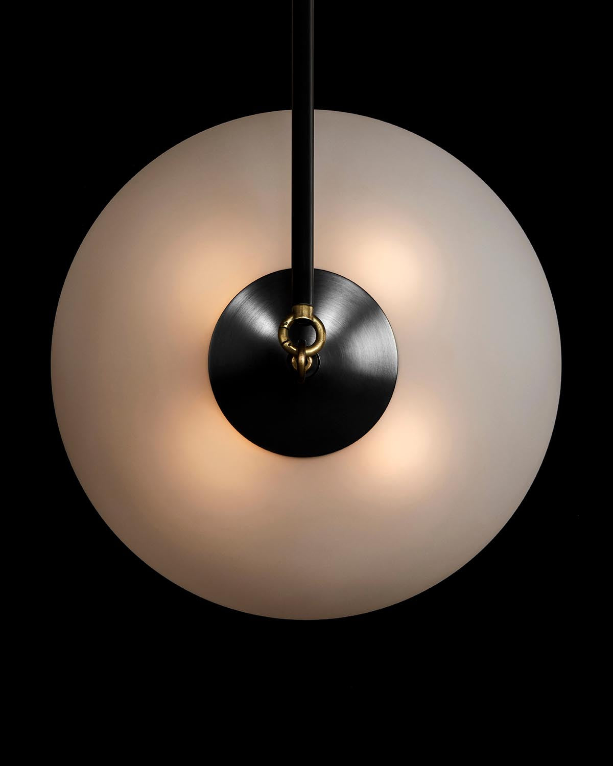 Overhead close-up of the SYNAPSE pendant light featuring a frosted glass globe and dark metal center detail on black background