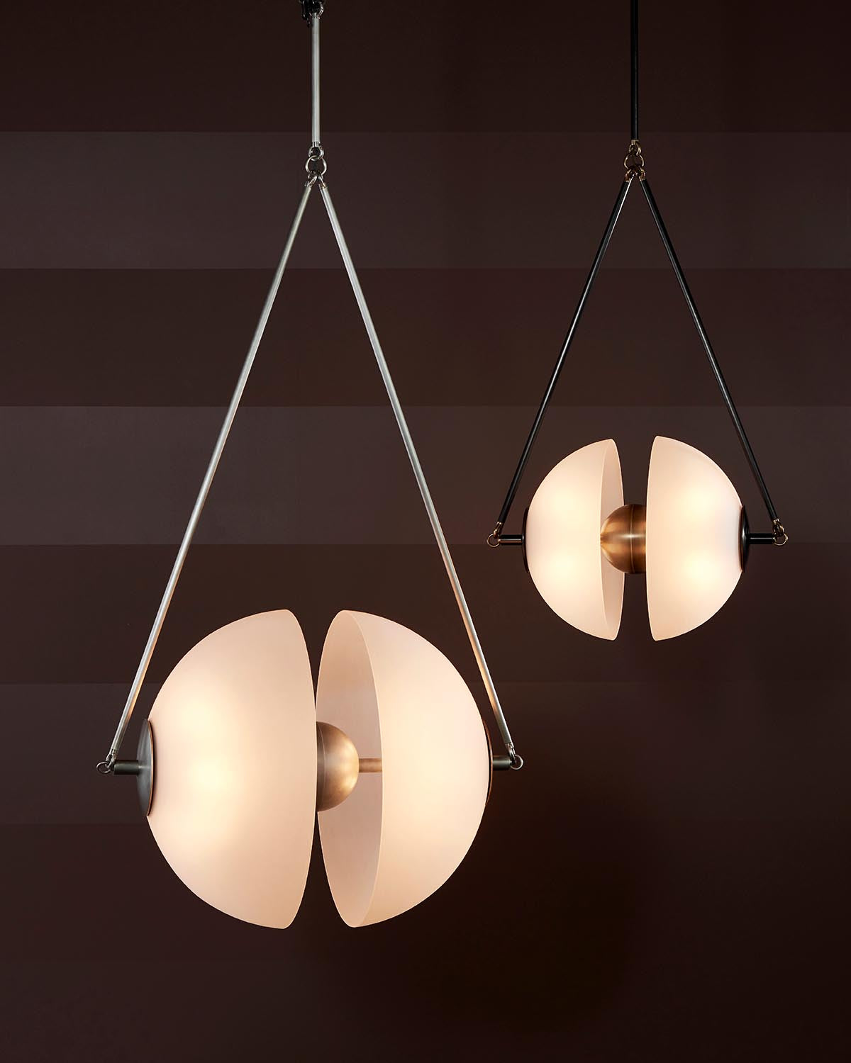 Two modern pendant lights with frosted curved glass shades and brass centers suspended by metal rods against a dark background