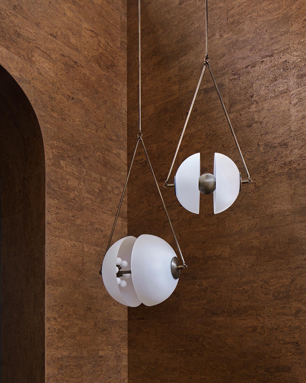 Two suspended pendant lights with matte white segmented globes and brushed metal accents against textured brown walls