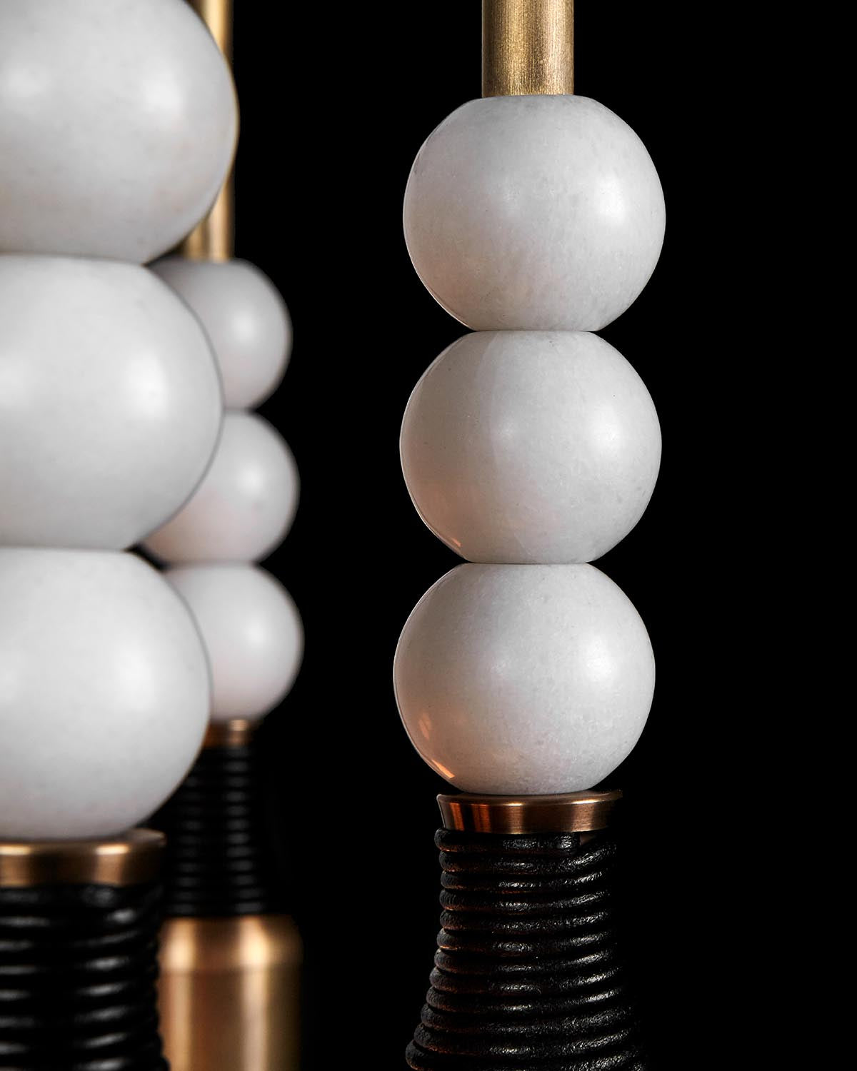 Close-up of stacked white marble spheres on a gold rod with a textured black and gold base against a black background