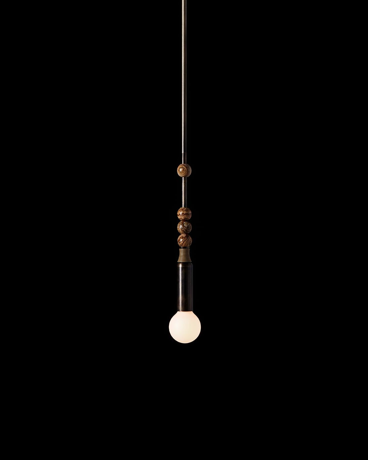 Minimalist pendant light with spherical wooden accents and a glowing bulb suspended by a thin dark cord on black background