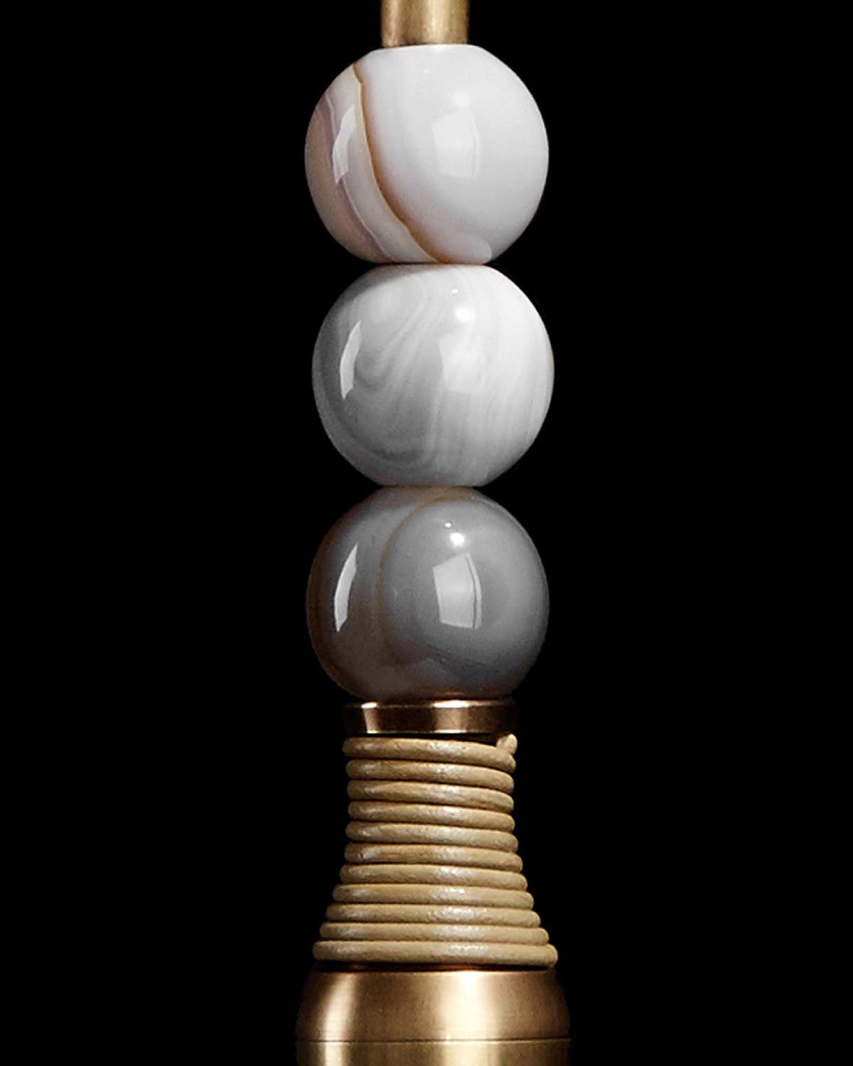 Close-up of TALISMAN pendant featuring three polished stone beads stacked on a gold-toned textured metal base against black background