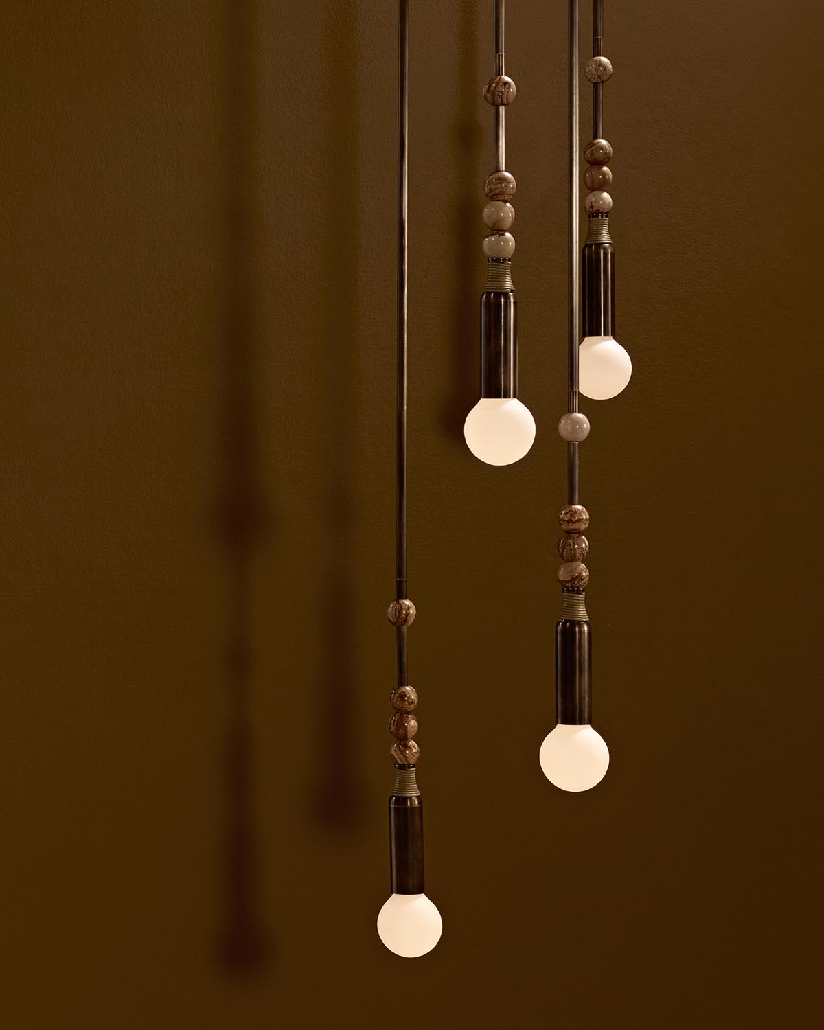 Three pendant lights with round frosted bulbs and decorative brown beads hanging against a warm brown background