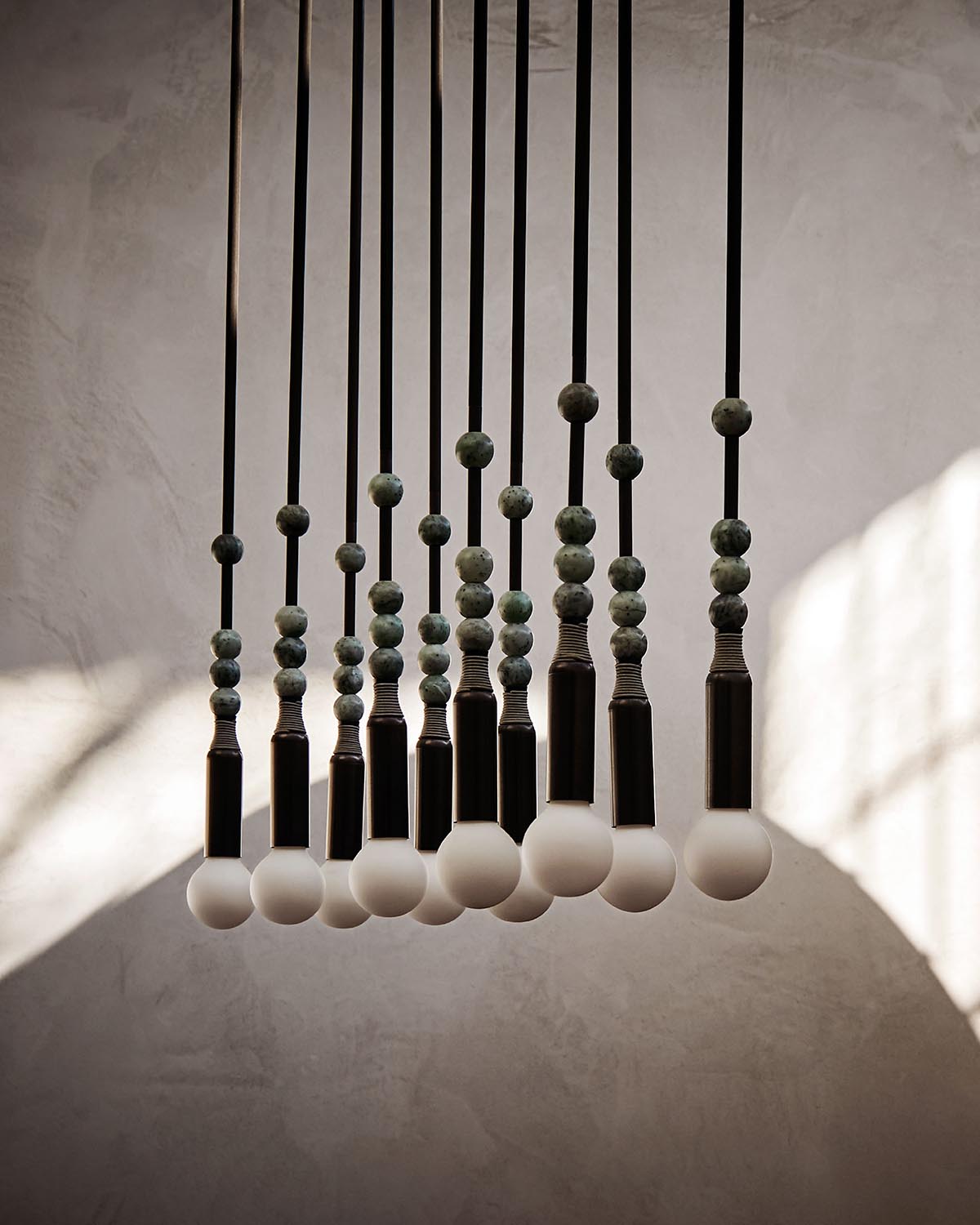 Group of pendant lights with frosted round bulbs and stacked greenish decorative beads on black cords against a textured wall