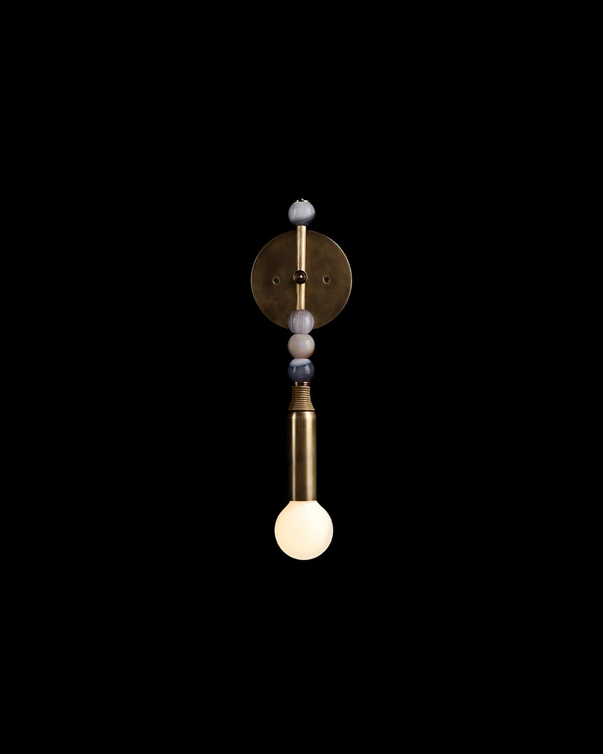 Wall-mounted light fixture with brass finish and agate stone accents above an exposed glowing bulb on black background