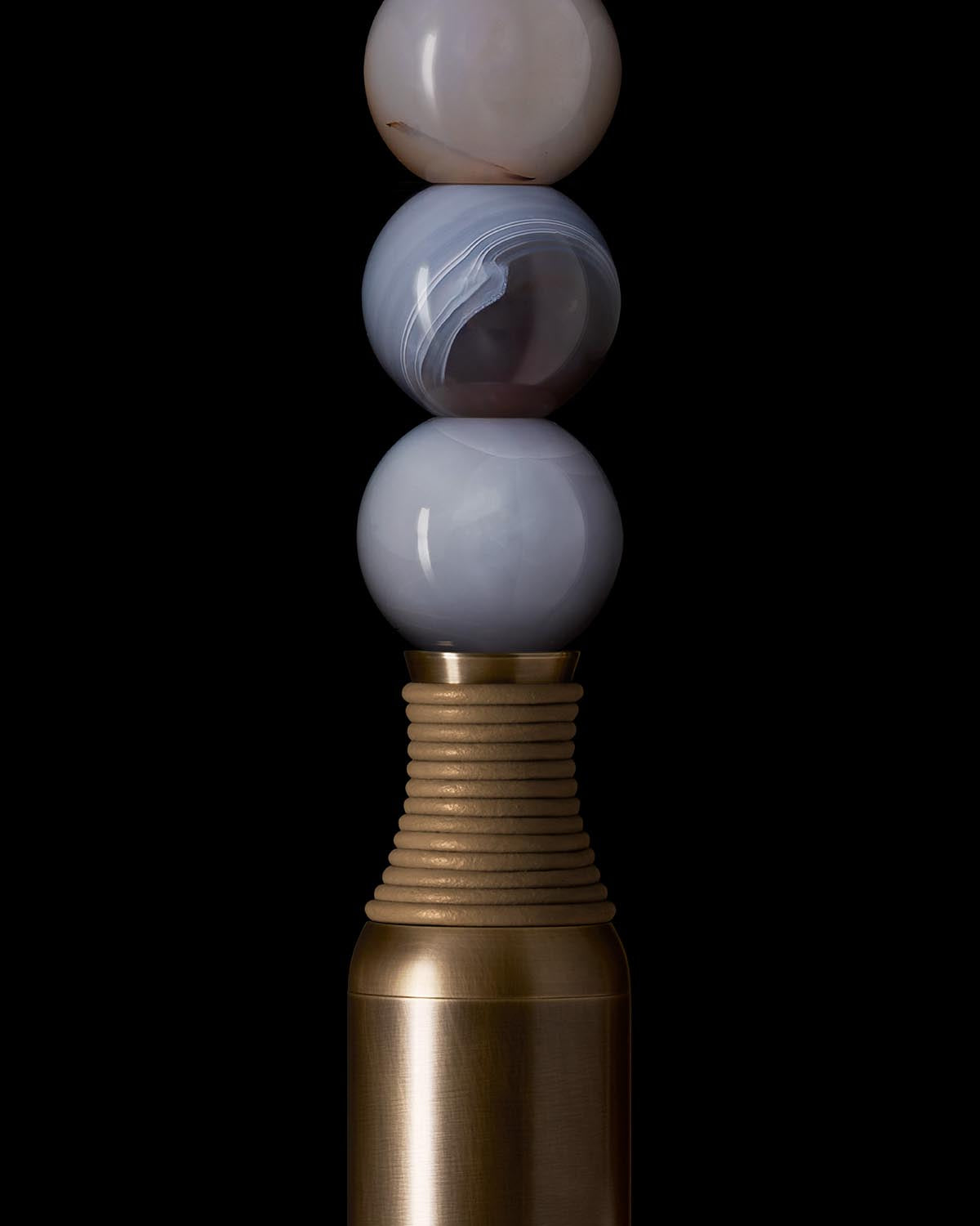 Close-up of stacked polished agate spheres above ribbed brass and matte bronze base on black background