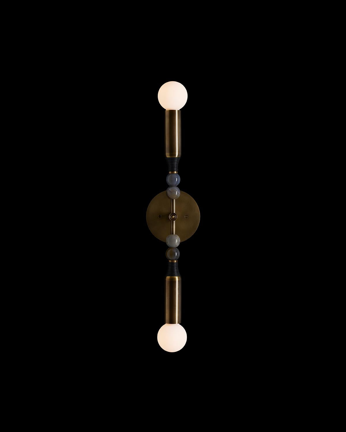 Vertical brass wall sconce with two opal glass globe bulbs and decorative spherical accents on black background