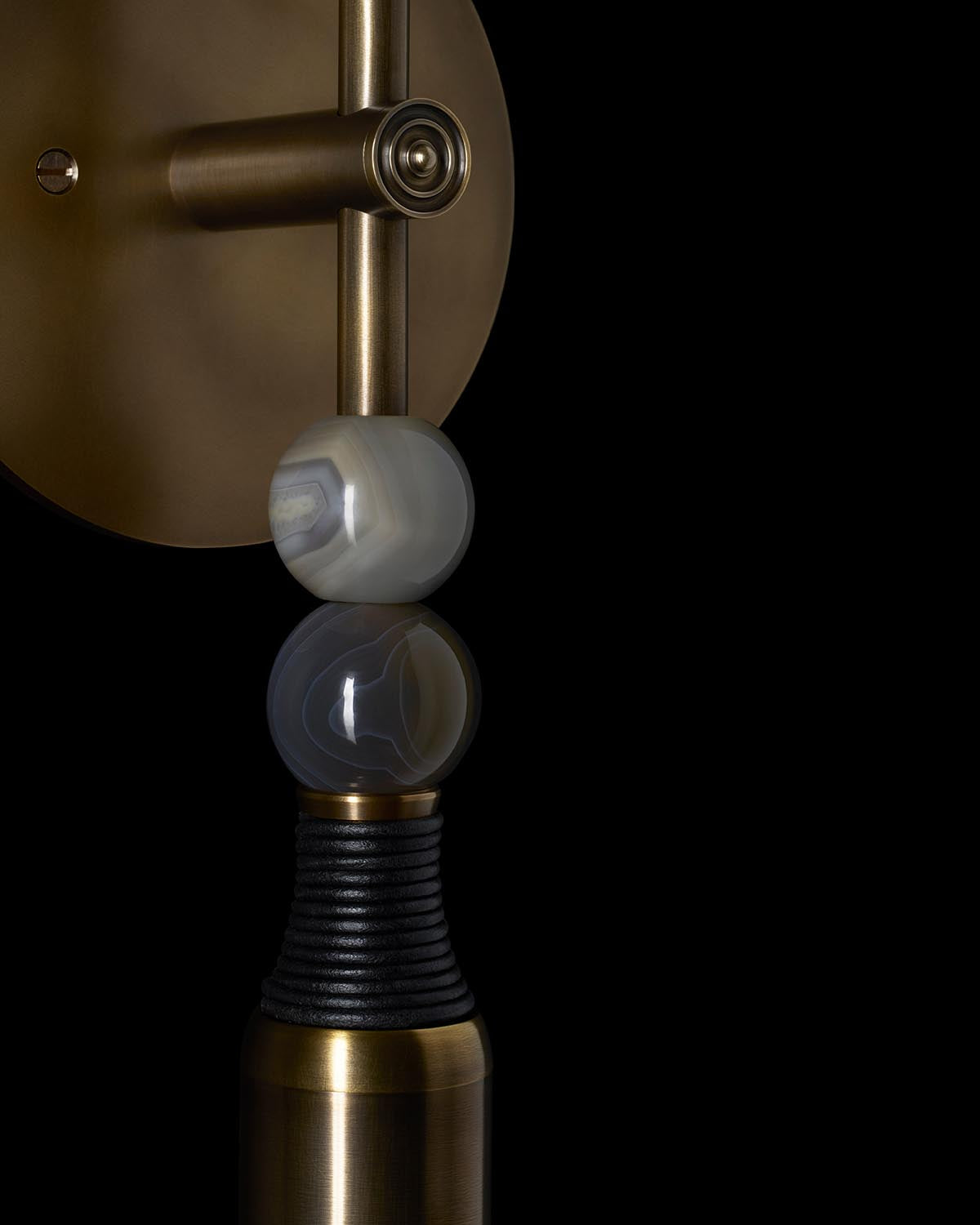 Close-up of a brass wall sconce with two translucent stone orbs and black wrapped cord detail against a black background