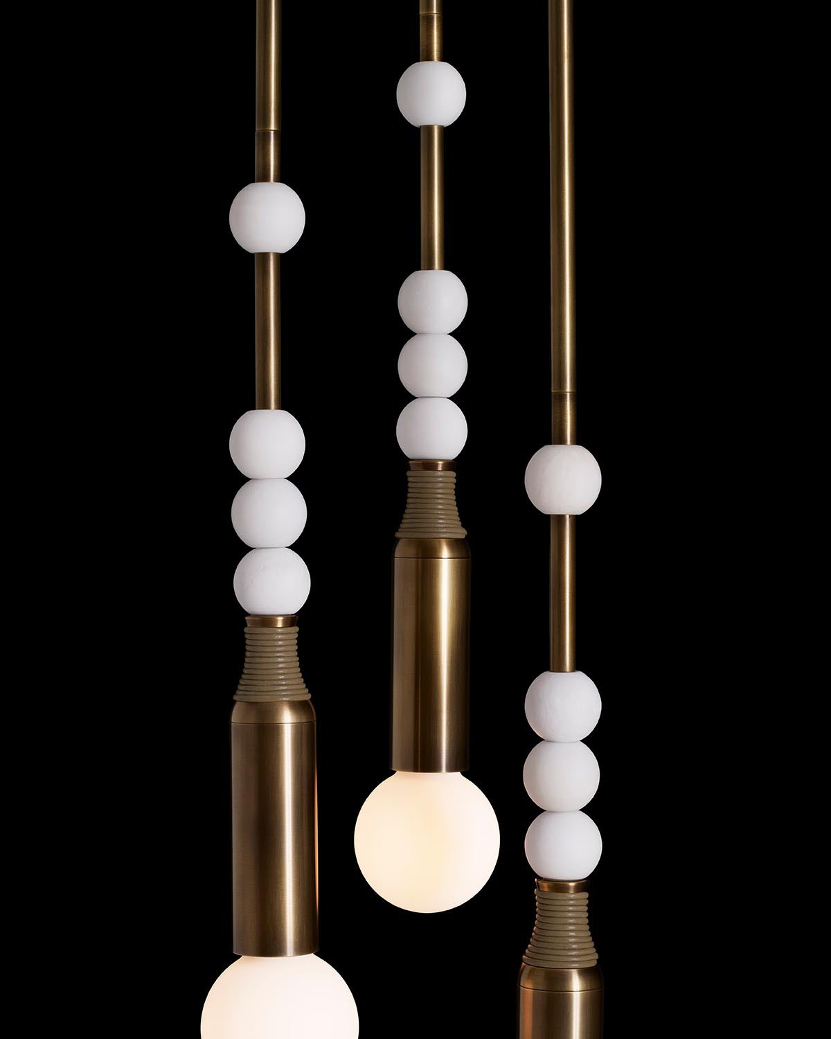 Close-up of three brass pendant lights with white spherical accents suspended against a black background