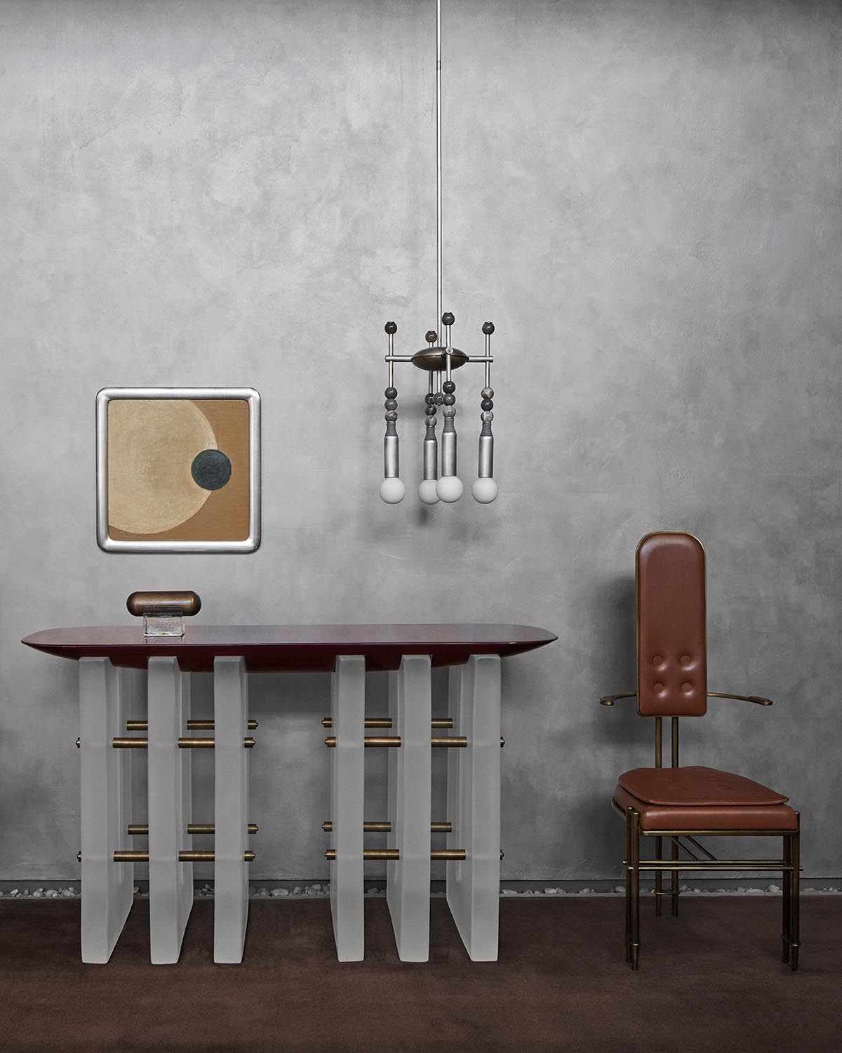 Modern console table with frosted vertical supports and dark wood top beside a brown leather chair under a sculptural pendant light