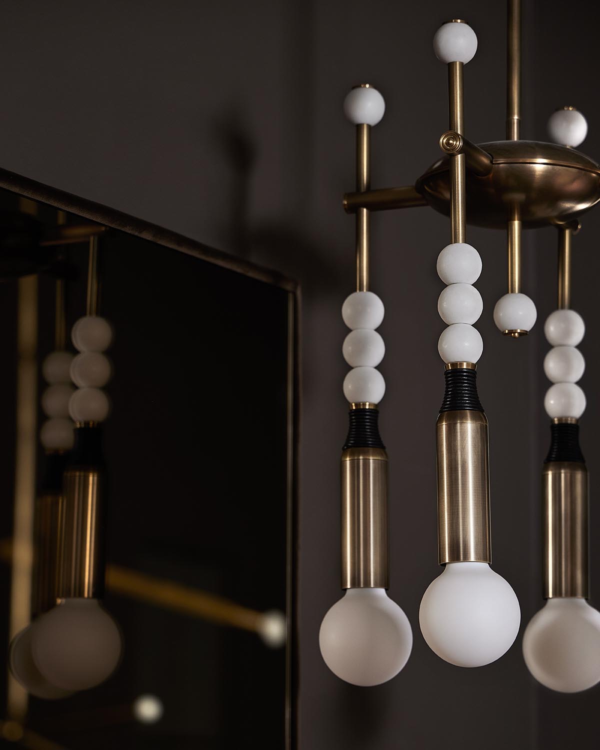 Close-up of a modern brass chandelier with white spherical bulbs and a reflective dark background