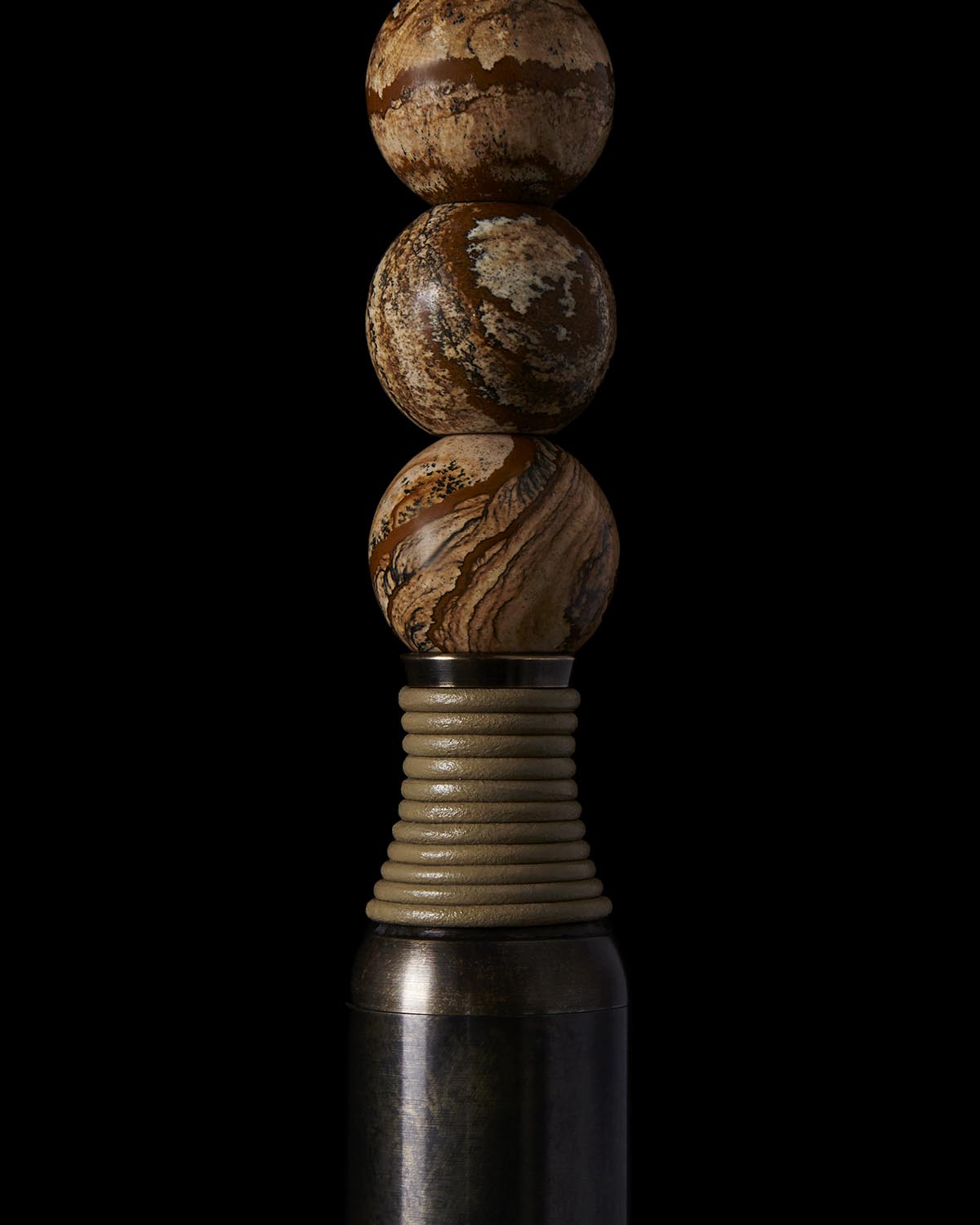 Stack of three textured brown marble spheres balanced on a ribbed cylindrical base with dark metal bottom on black background