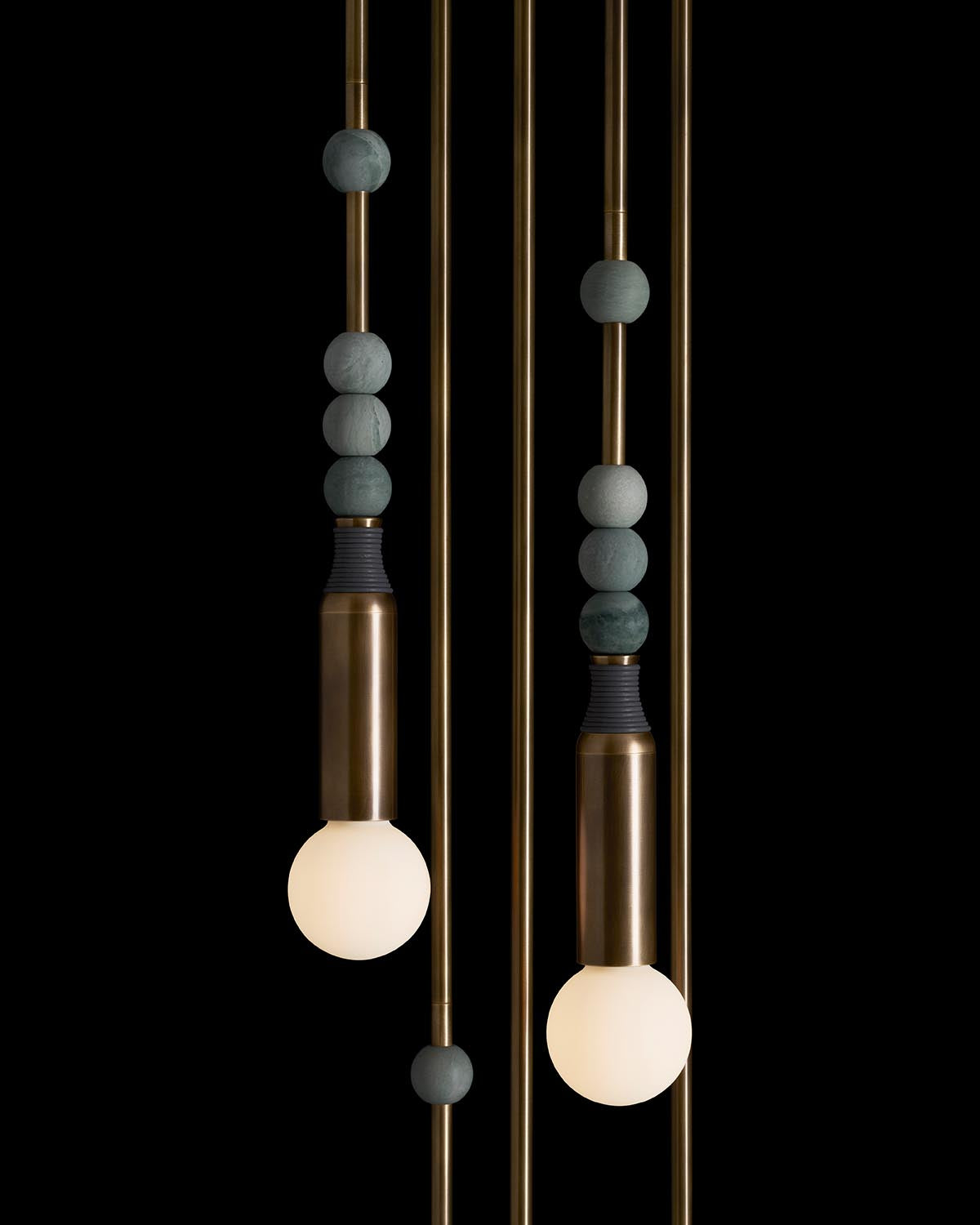 Close-up of modern pendant light installation with brass rods, matte stone spheres, and glowing round bulbs on black background