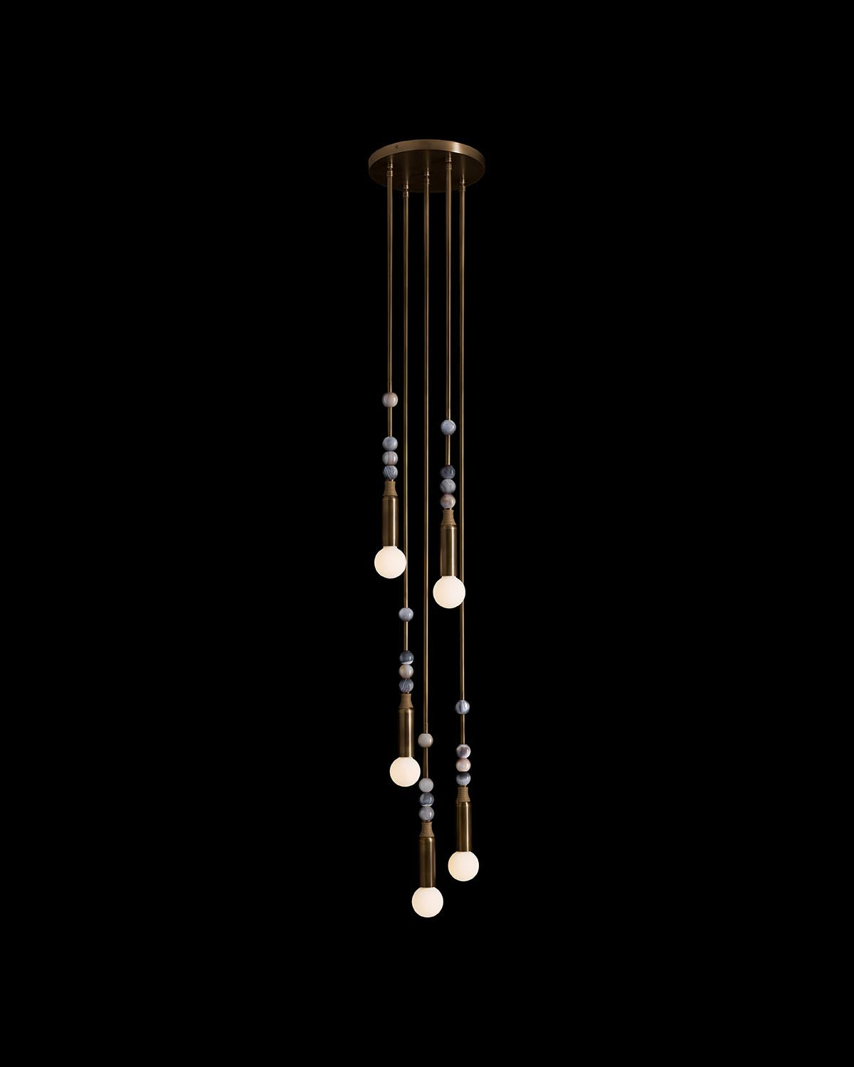 Hanging pendant light with five glowing bulbs suspended on brass rods adorned with natural stone beads against a black background