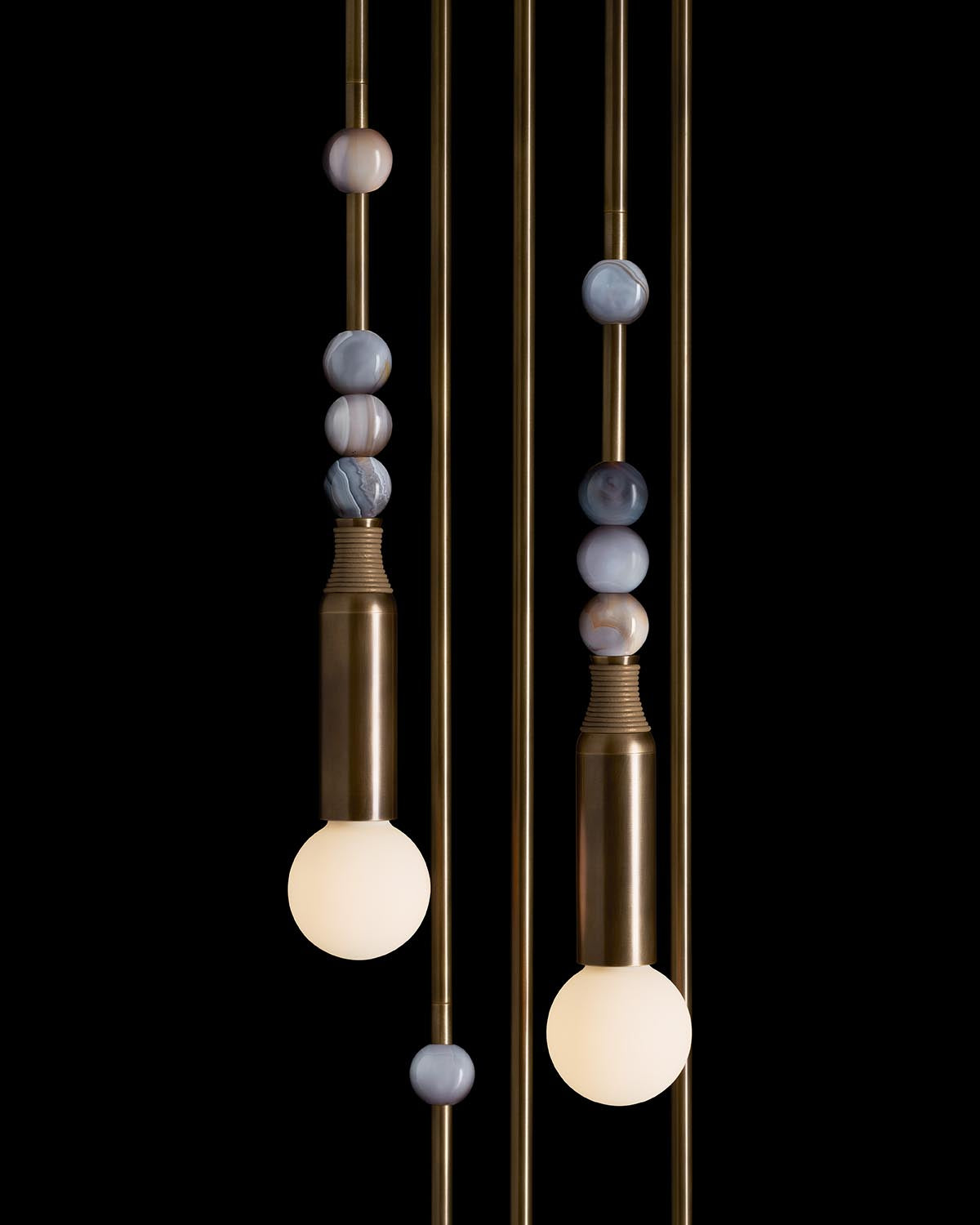 Two pendant bulbs with brushed brass sockets and natural agate stone beads on vertical rods against black background
