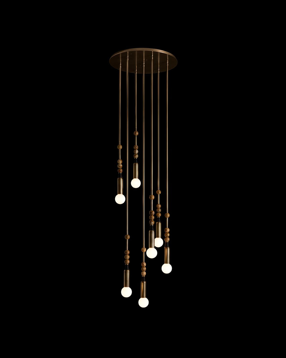 Modern pendant light installation with multiple cylindrical brass fixtures and exposed round bulbs hanging on thin cords against black background