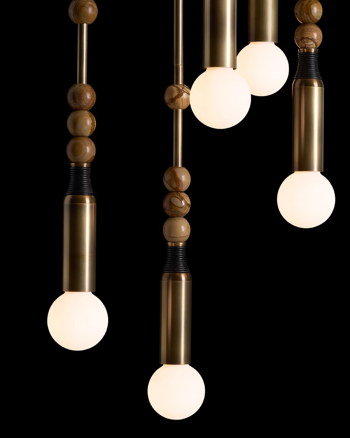 Close-up of four pendant lights with brass and wooden elements and frosted round bulbs on a black background