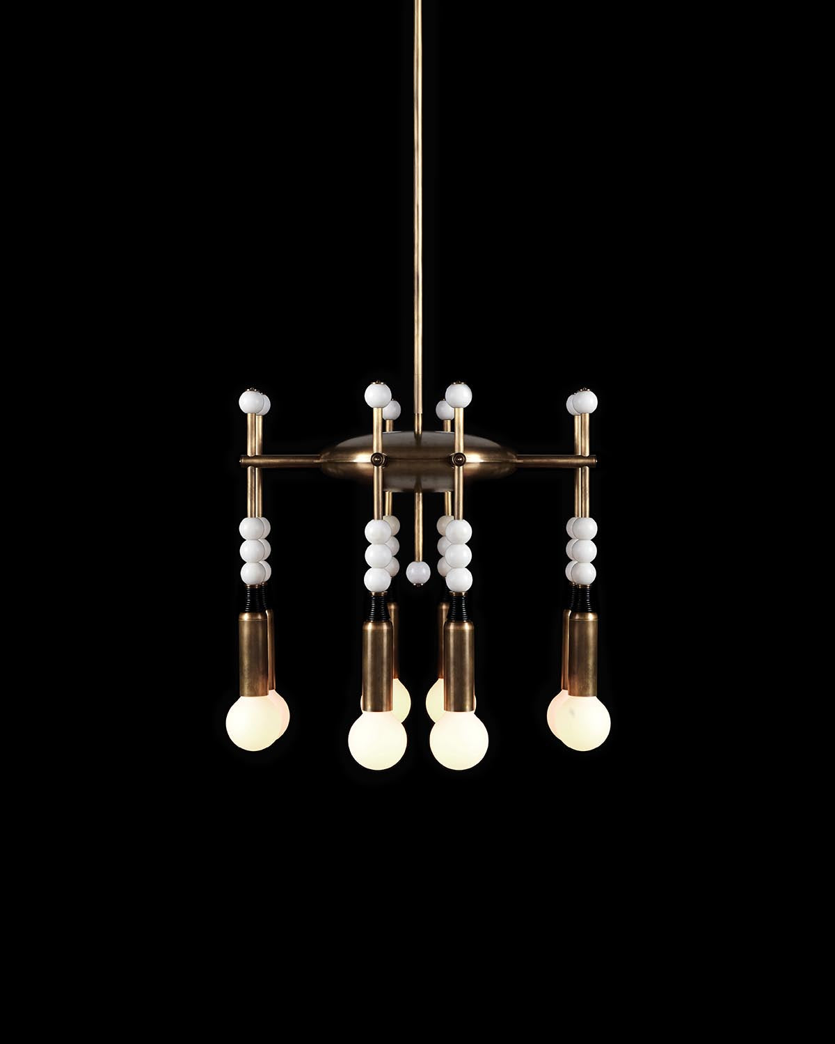 Suspended brass chandelier with four glowing round bulbs and decorative white bead accents on a black background