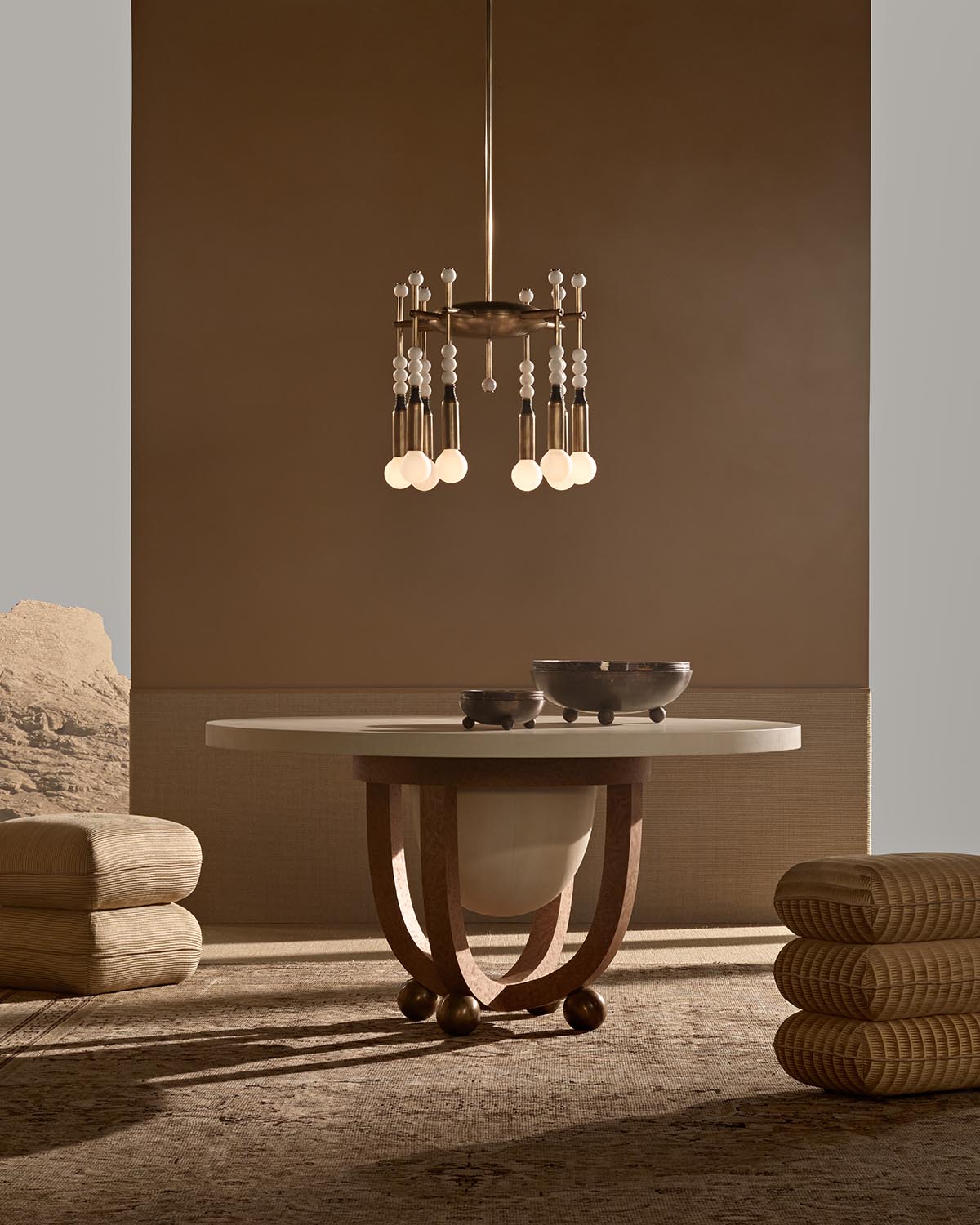 Modern round table with curved wooden legs and decorative bowls, illuminated by a suspended pendant light fixture.