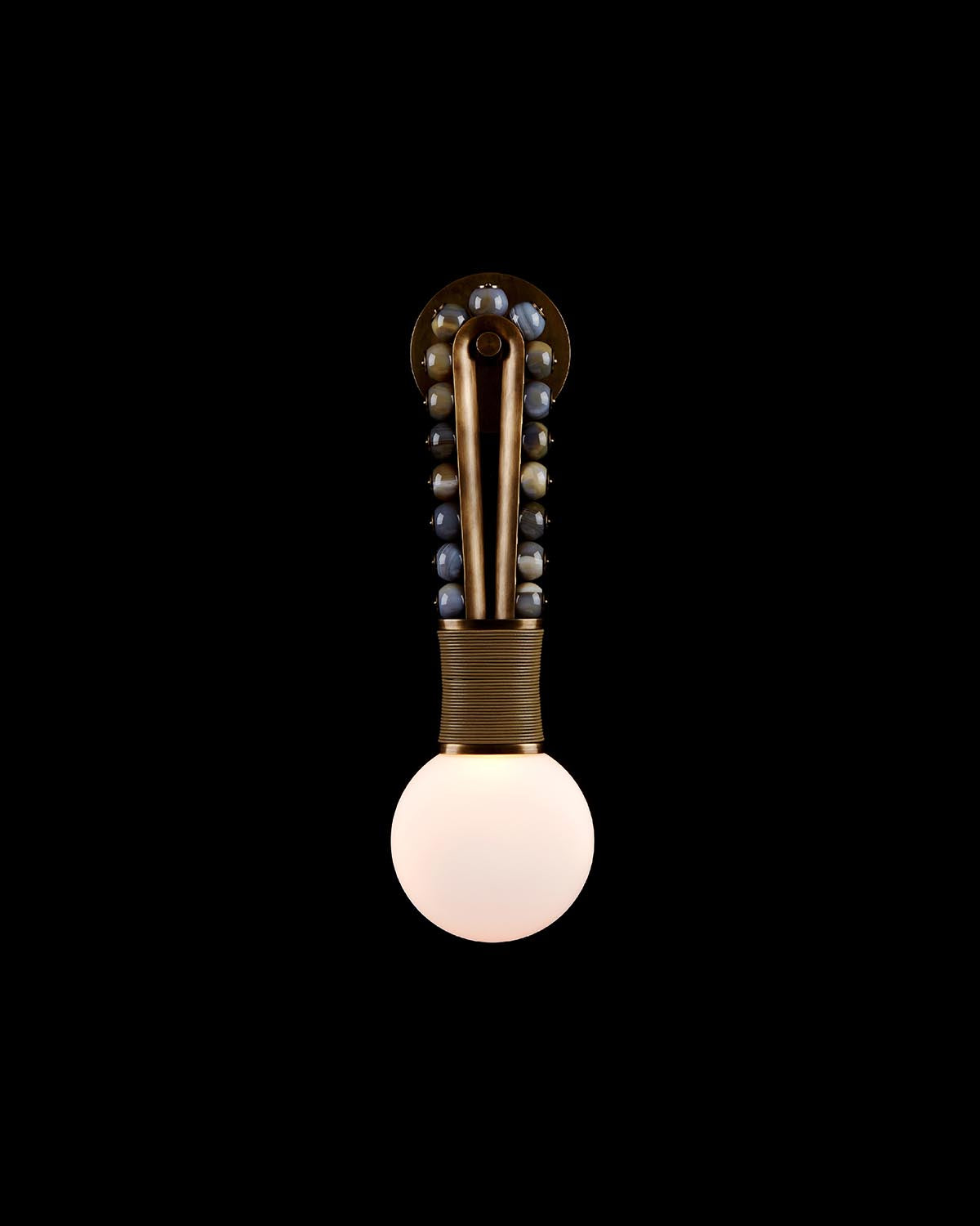 Vertical metal wall sconce with spherical light bulb and decorative round beads on dark background