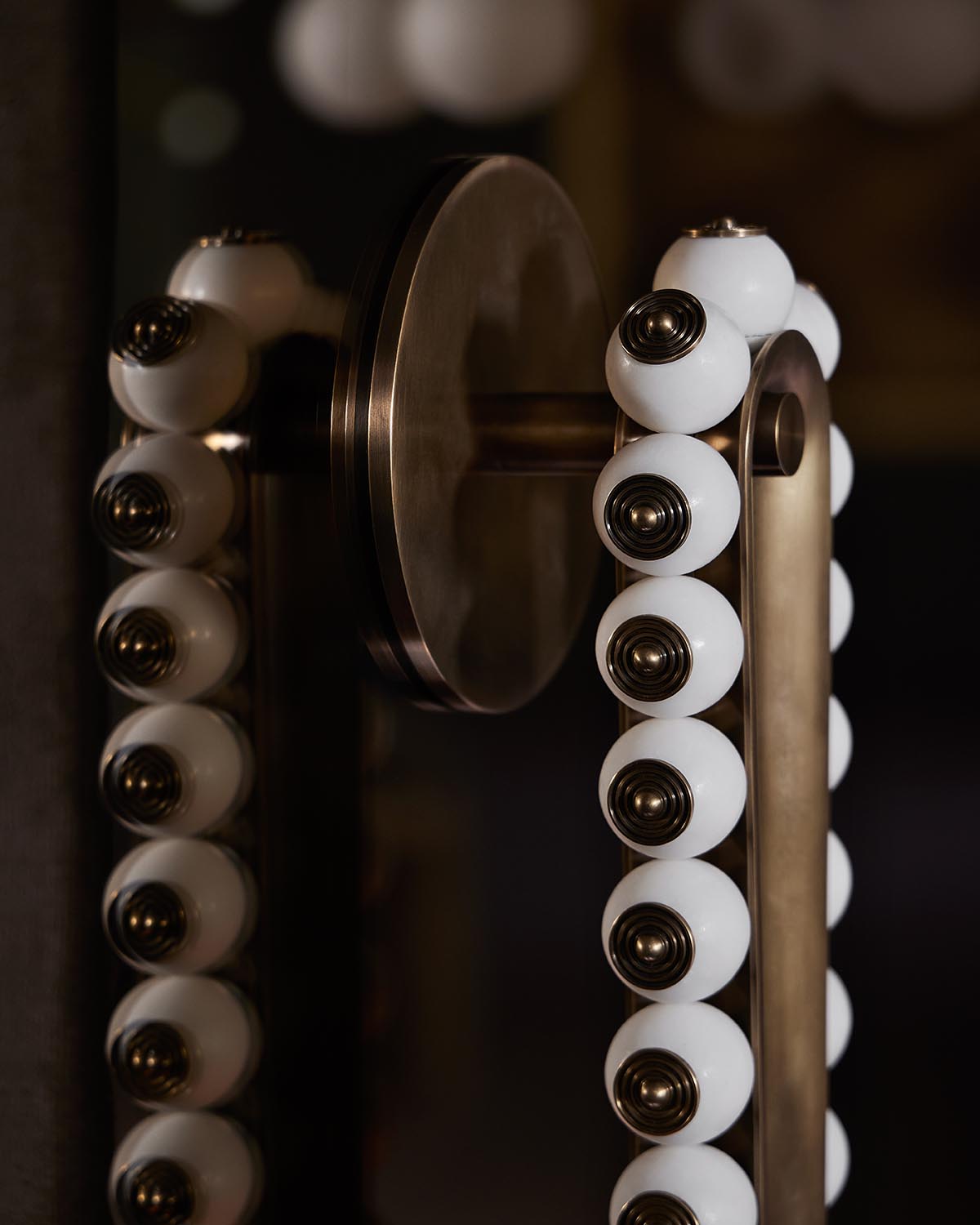 Close-up of TALISMAN Loop Sconce with white globe bulbs and antique brass finish on dark background