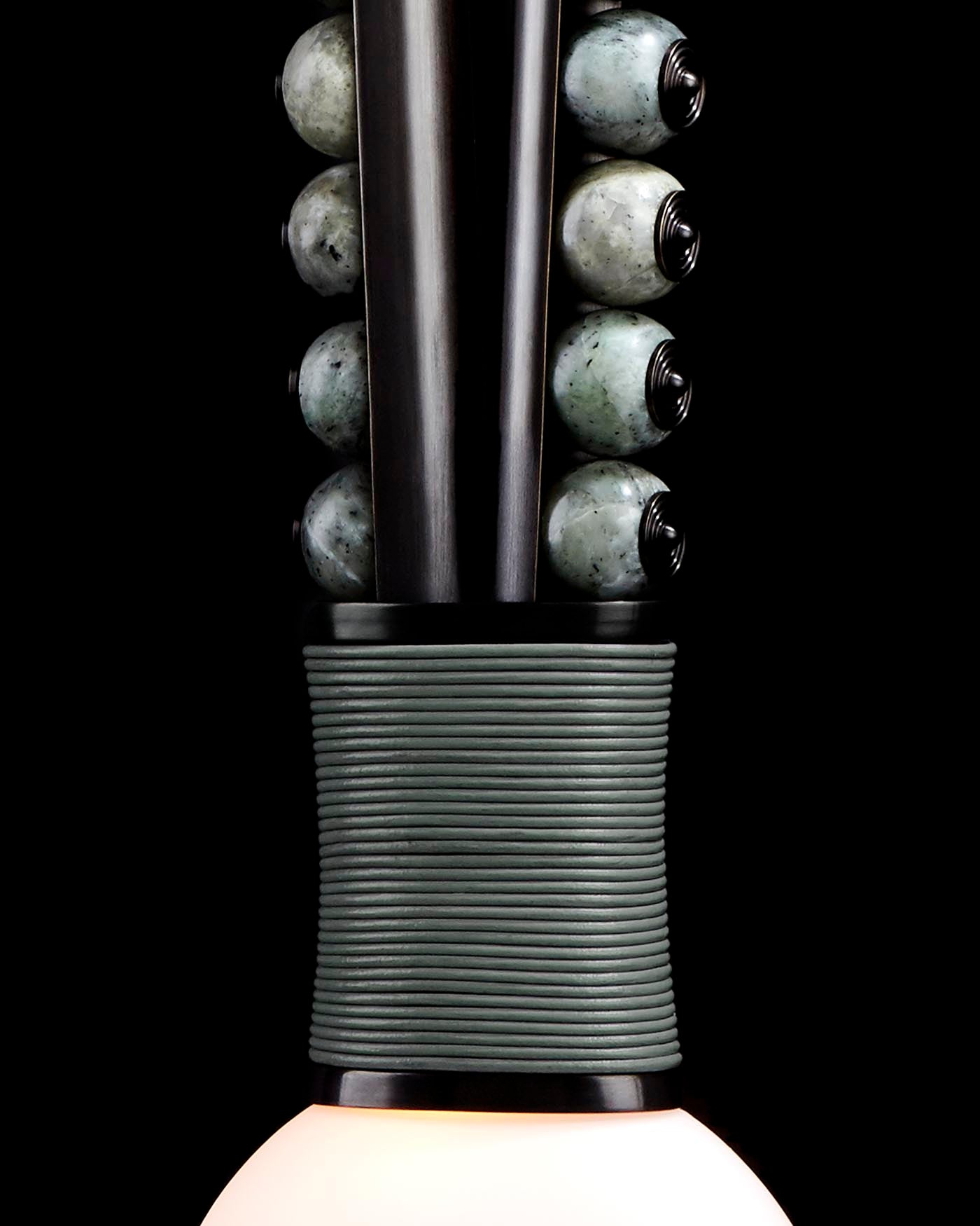 Close-up of a modern sconce with black metal frame, wrapped cord detail, and round stone beads against a black background