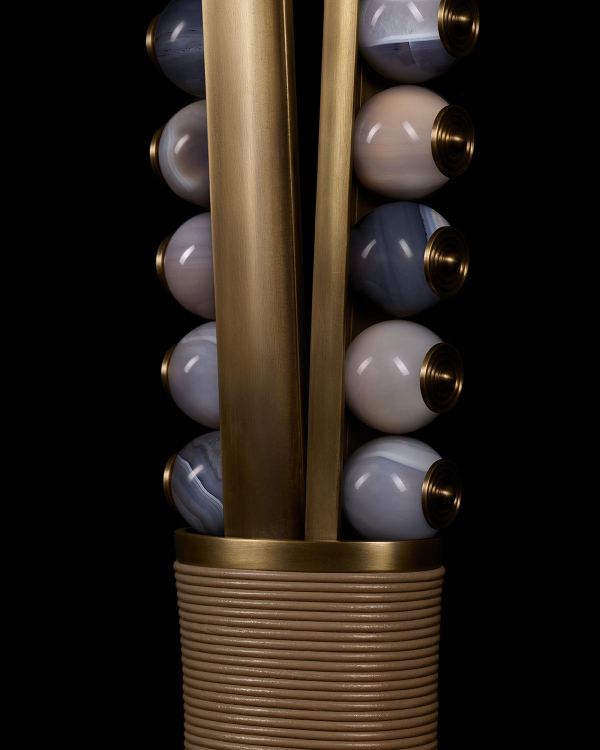 Close-up of tall brass fixture with alternating banded agate spheres in tan and gray tones on black background