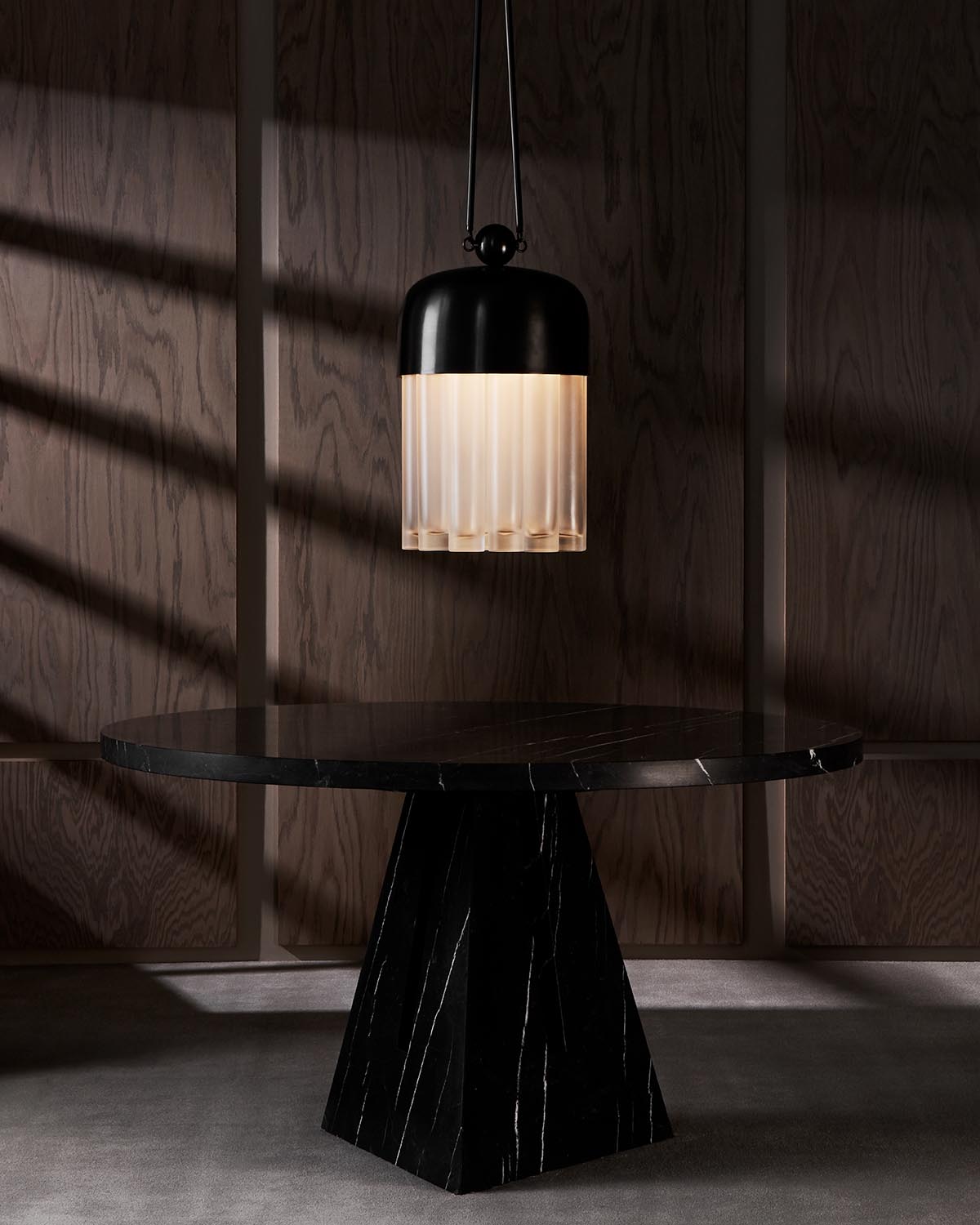 Pendant lamp with ribbed frosted glass shade and matte black top hanging above a round black marble table in a dark wood paneled room