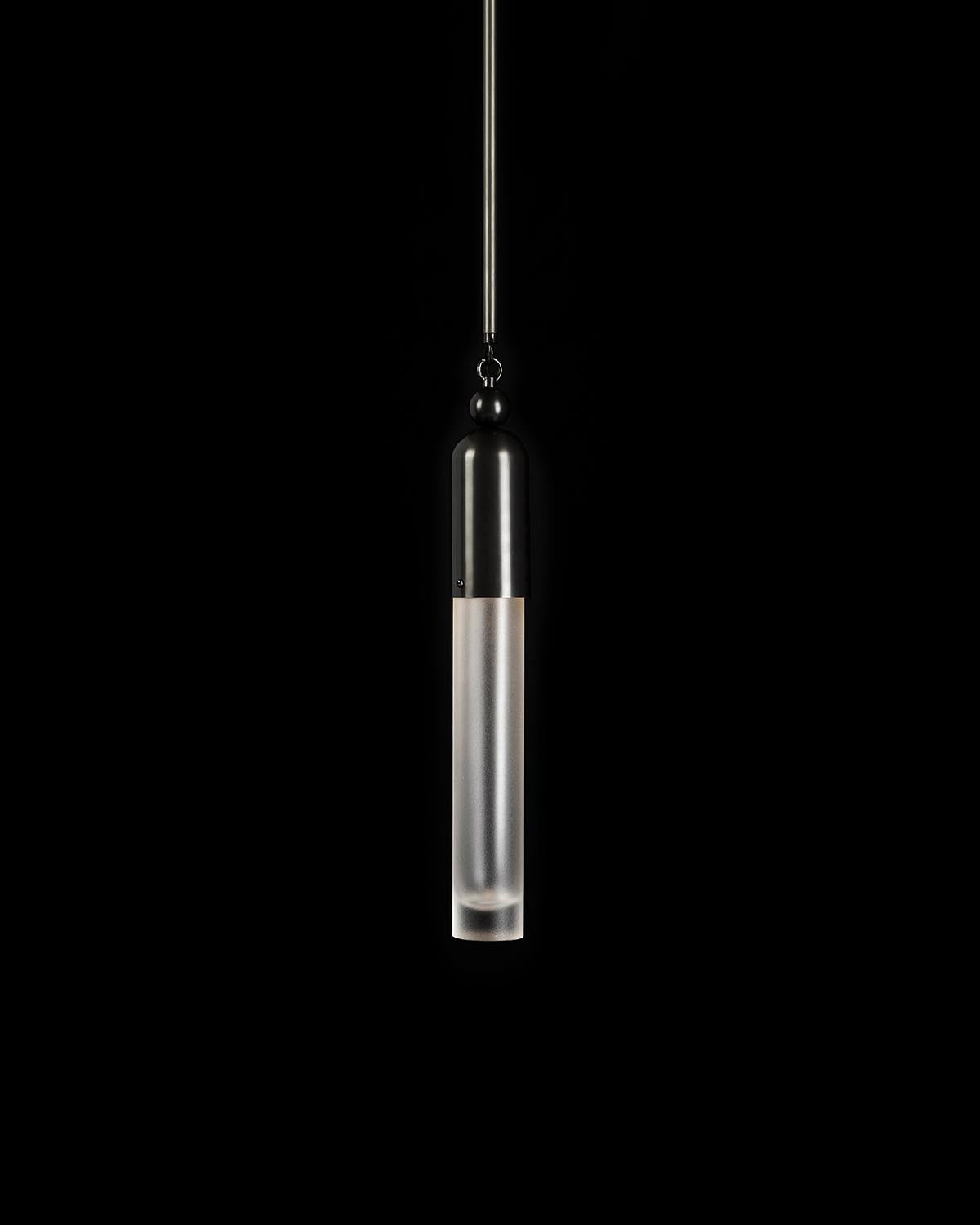 Minimalist cylindrical pendant light with frosted glass bottom and metal rod suspension against a black background