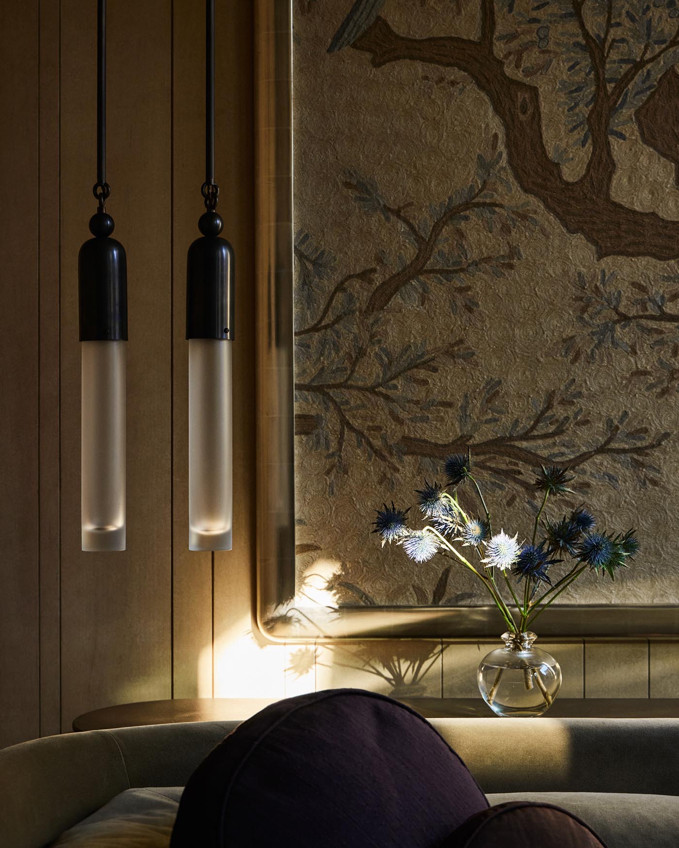 Two minimalist pendant lights with frosted glass and black caps hanging beside a textured wall with floral decor in soft lighting