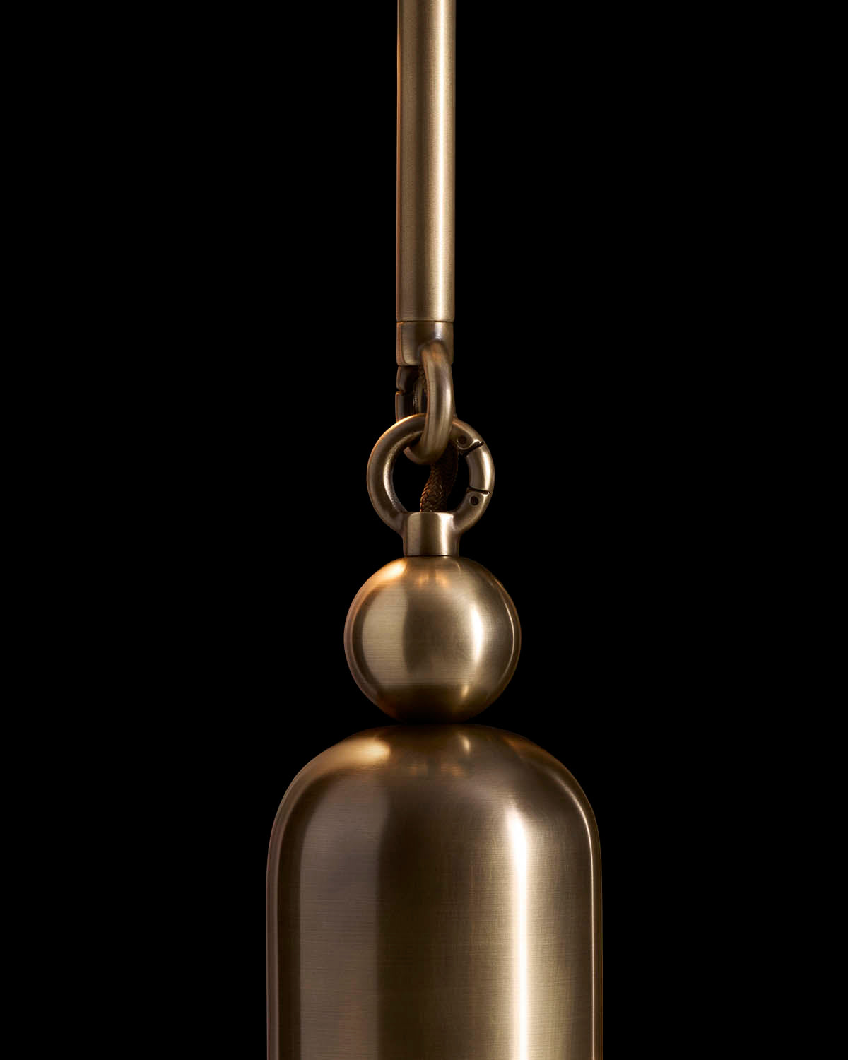 Close-up of a bronze pendant tassel with smooth rounded shapes hanging against a black background
