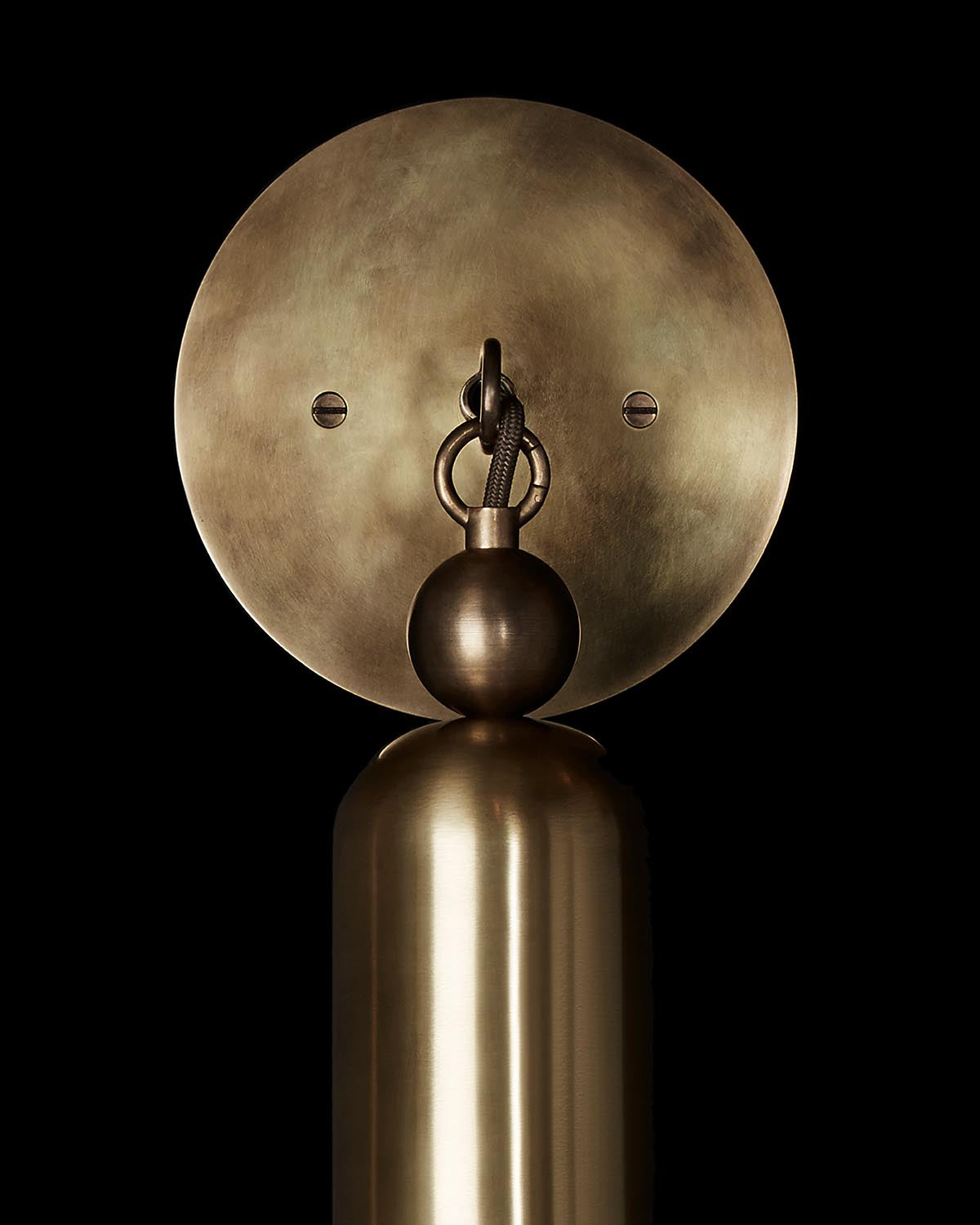 Close-up of a metallic wall sconce with circular backplate and cylindrical base against a black background