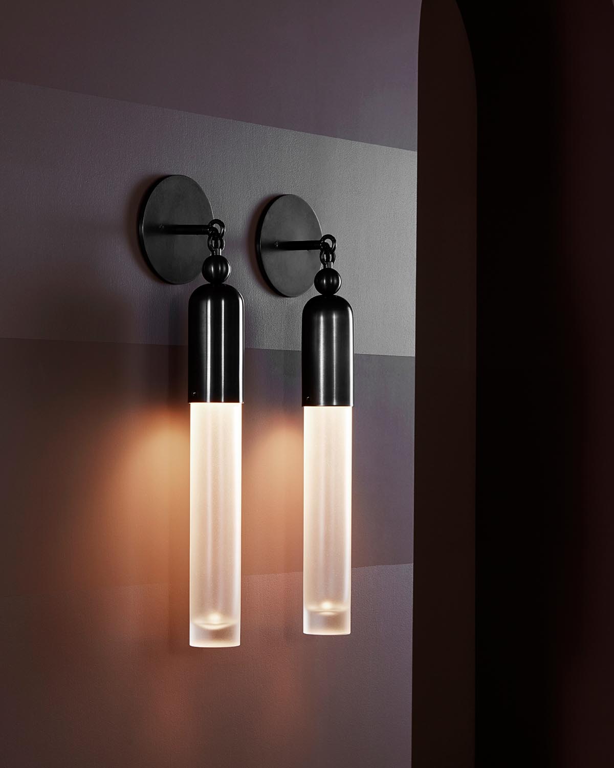 Pair of modern black metal sconces with elongated frosted glass shades mounted on a muted purple striped wall