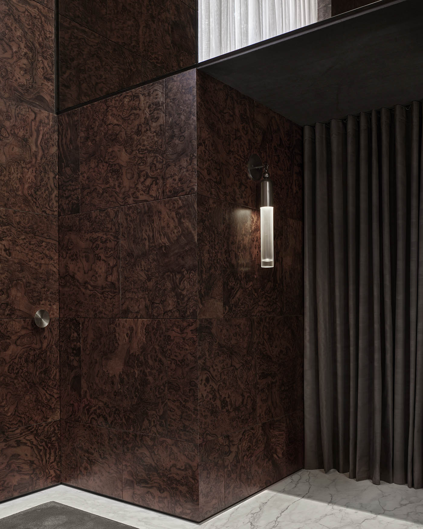 Minimalist cylindrical wall sconce with frosted glass and metal mount on dark textured wood-paneled corner wall