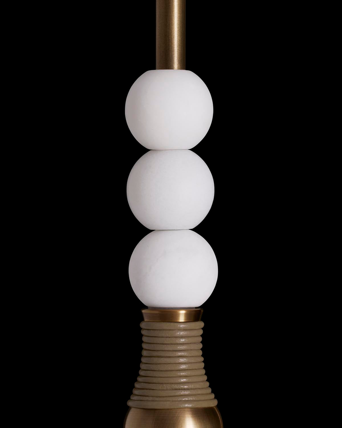 Close-up of TALISMAN 1 wall sconce featuring three stacked white globe lights and brass accents on black background