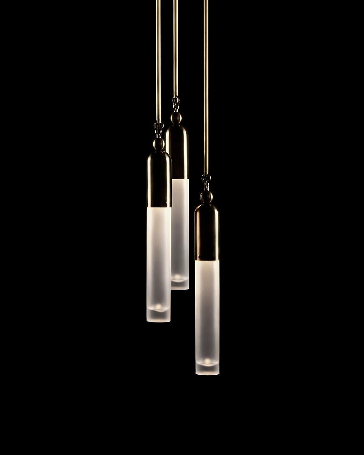 Three vertical cylindrical pendant lights with frosted glass and brass accents hanging against a black background