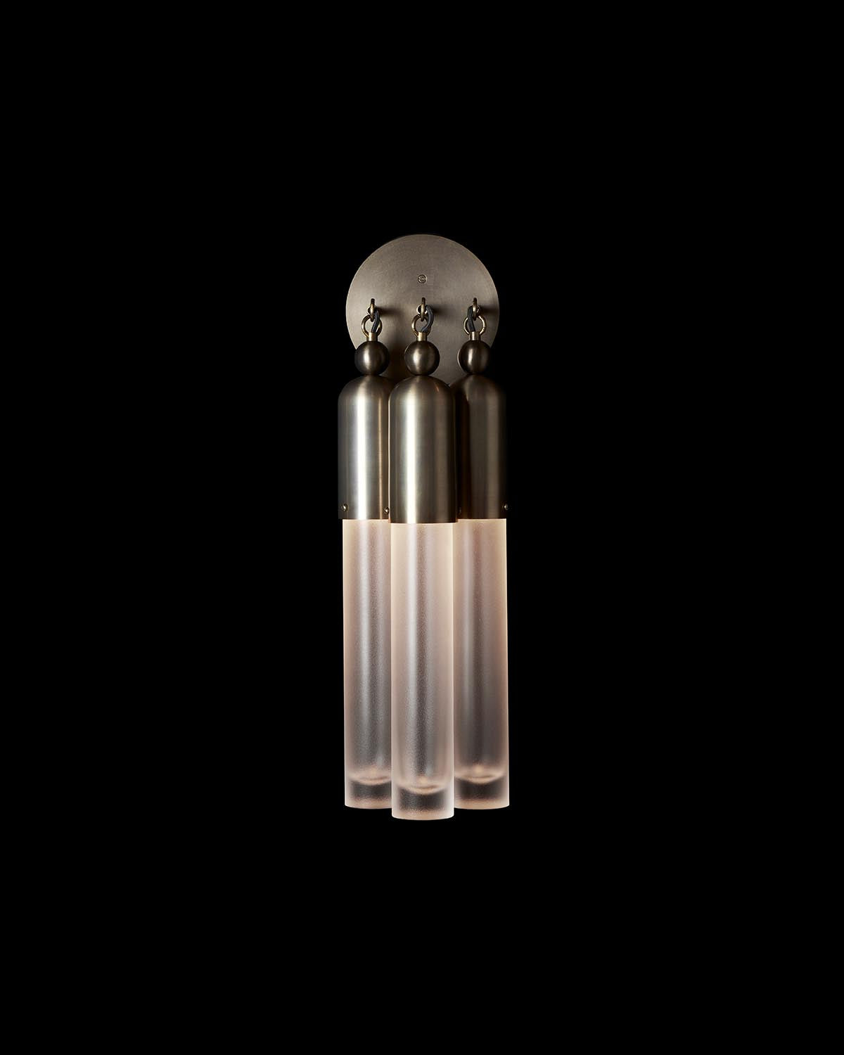 Close-up of a modern triple sconce with frosted glass tubes and metallic tops against a black background