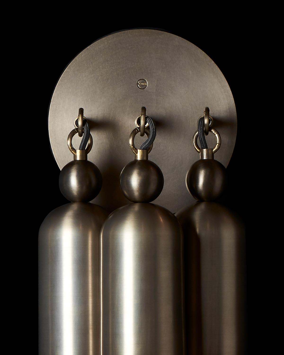 Close-up of a metallic triple sconce light fixture with cylindrical bulbs and round backplate against a black background